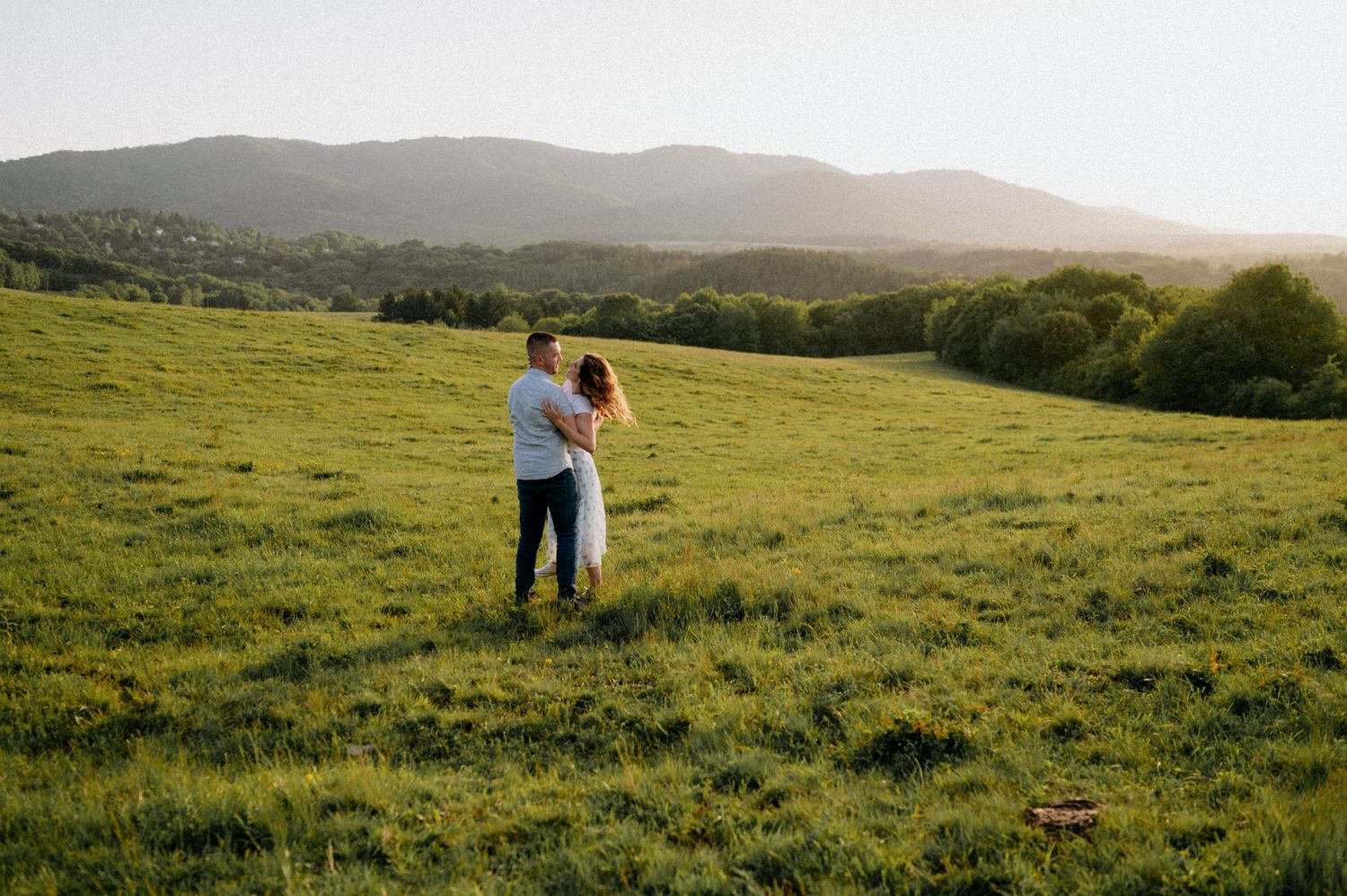 A couple shares an intimate moment in a mountain meadow during golden hour.