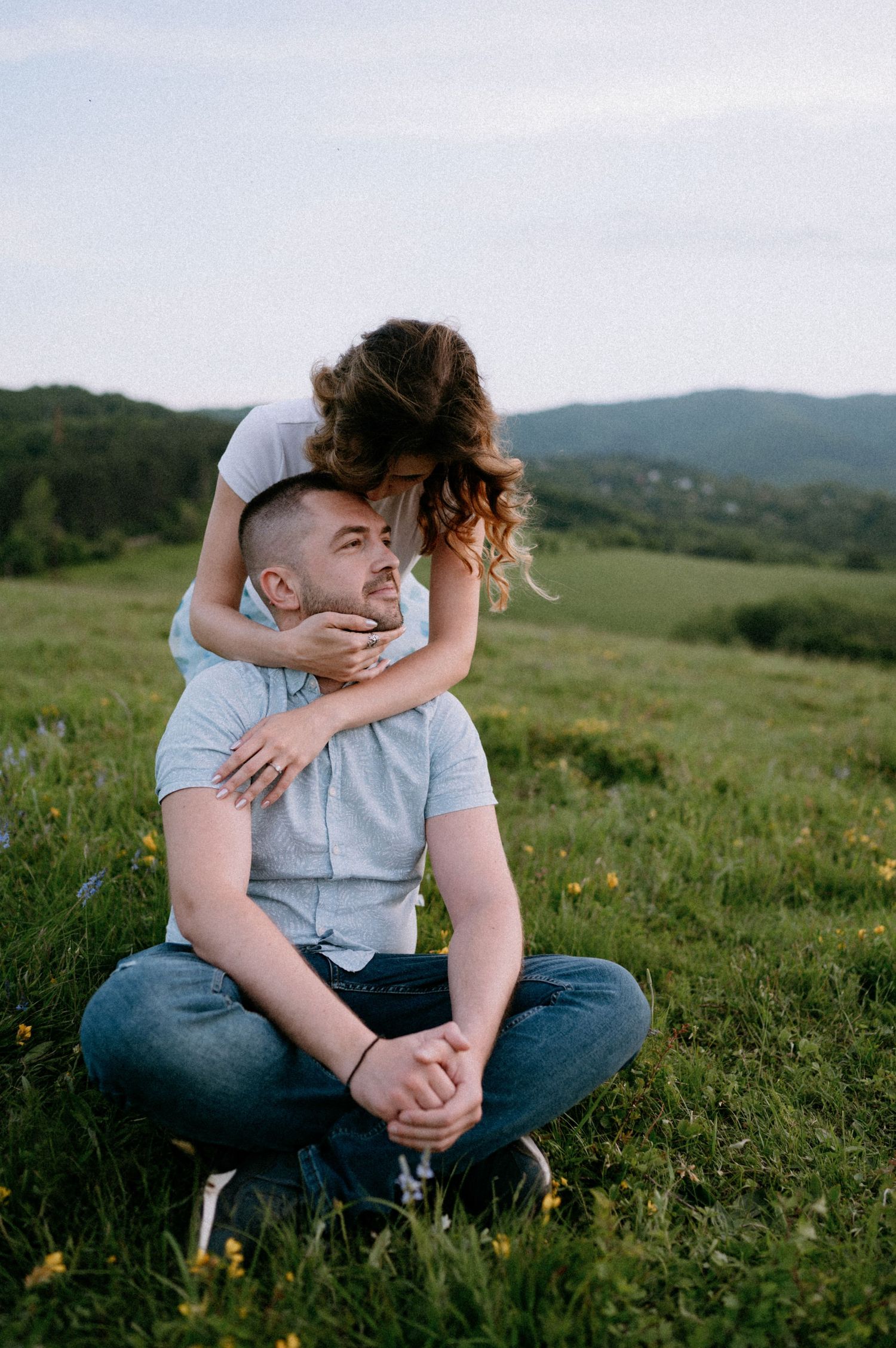 An intimate moment captured between two people sitting in a flower-filled mountain meadow.