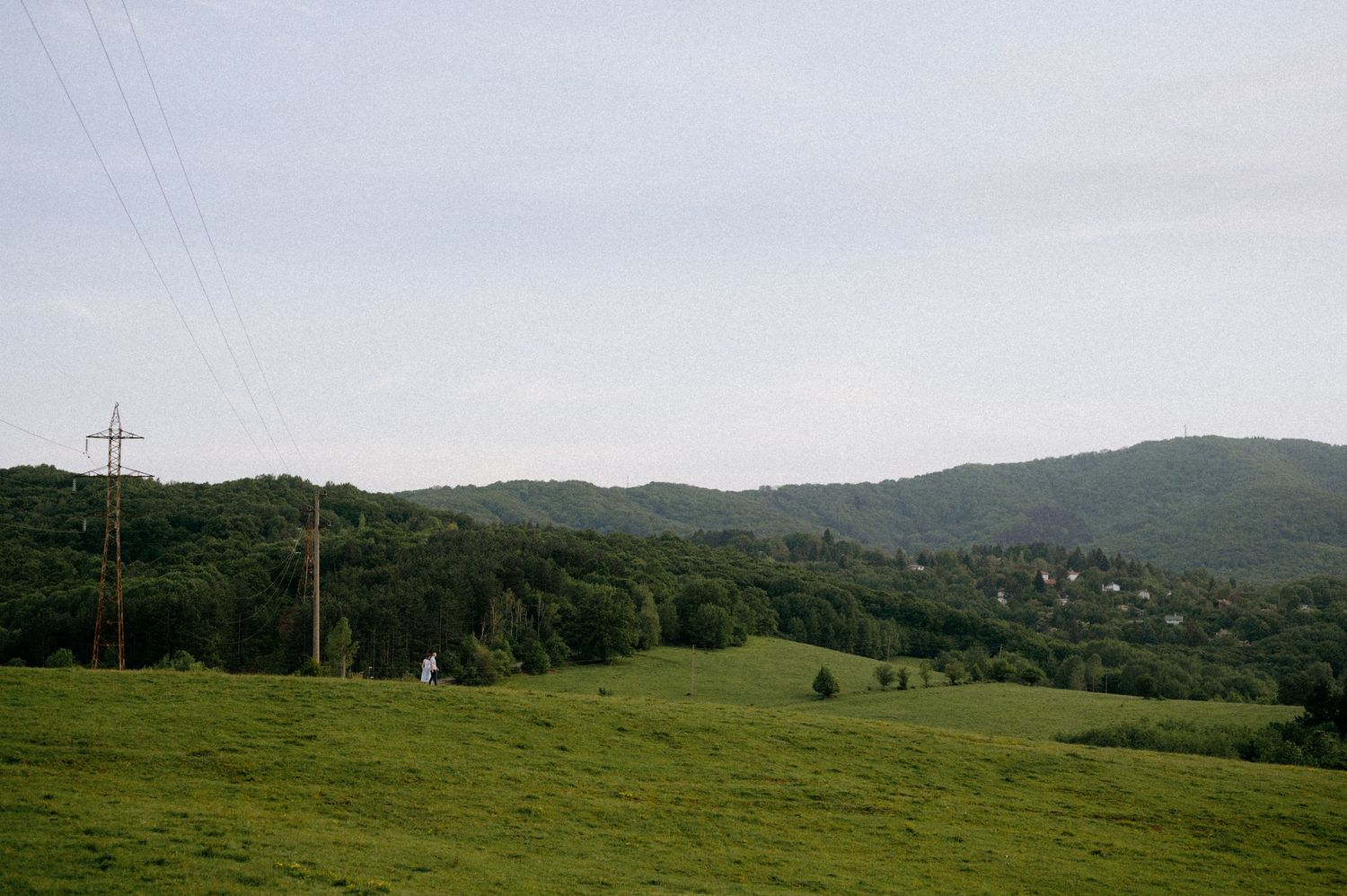 Mountain landscape with electrical towers and lines stretching across green pastures.