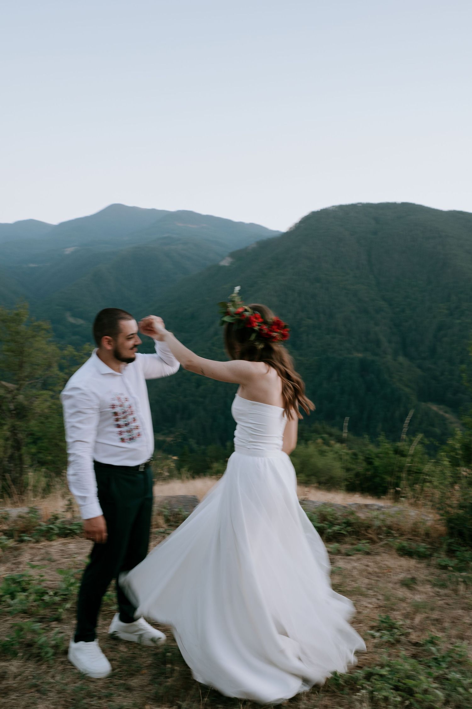 Dancing together in wedding attire on a mountain ridge with valley views.