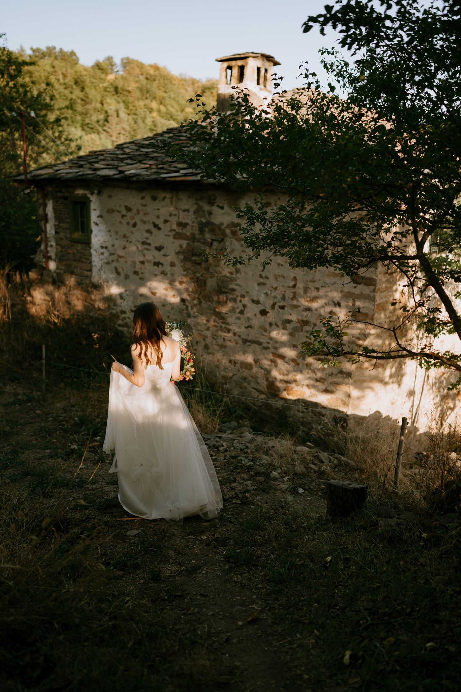 Stone wall structure nestled among trees at sunset creating dramatic shadows.