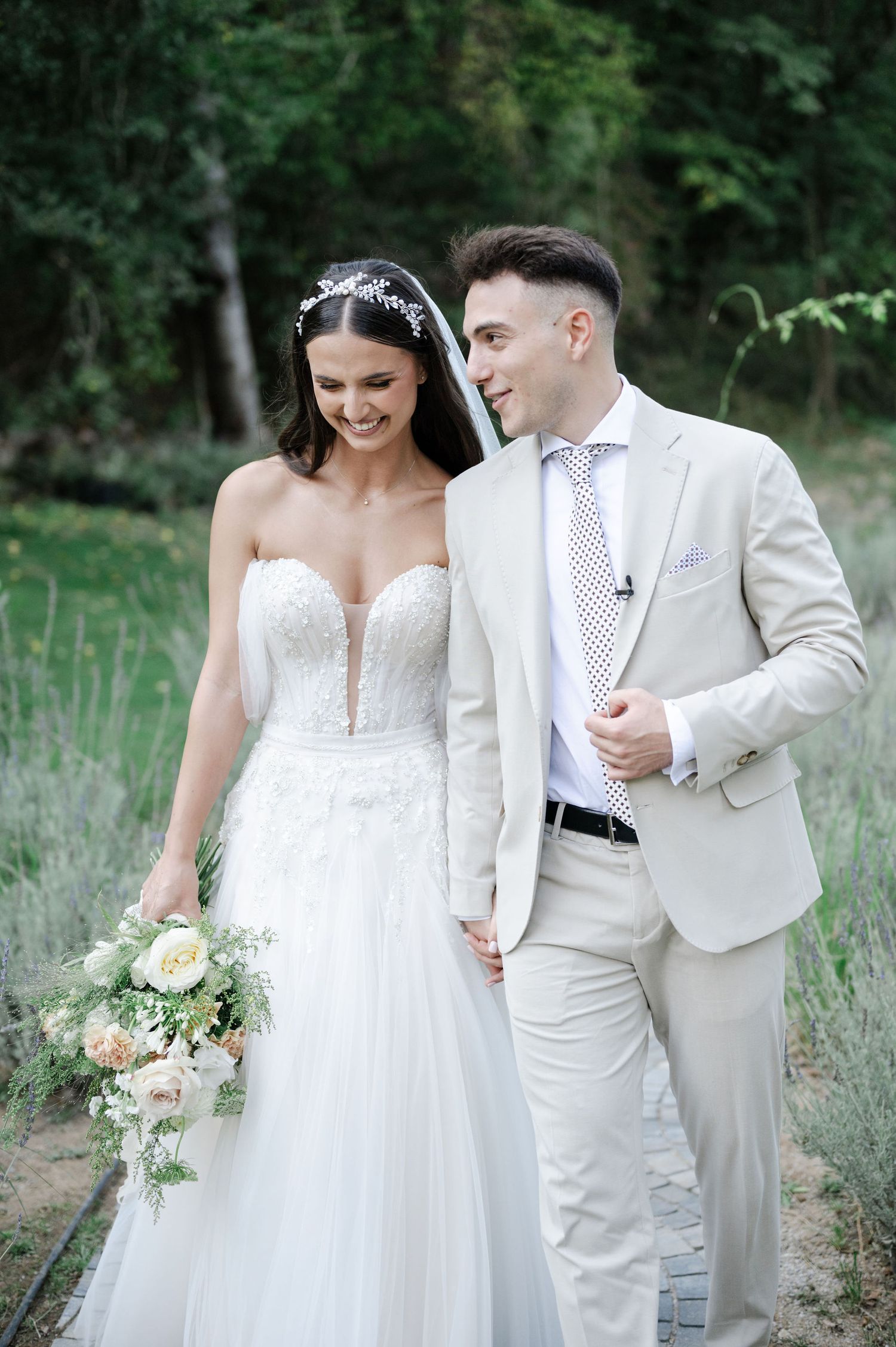Candid wedding photo of couple walking outdoors among lavender plants.