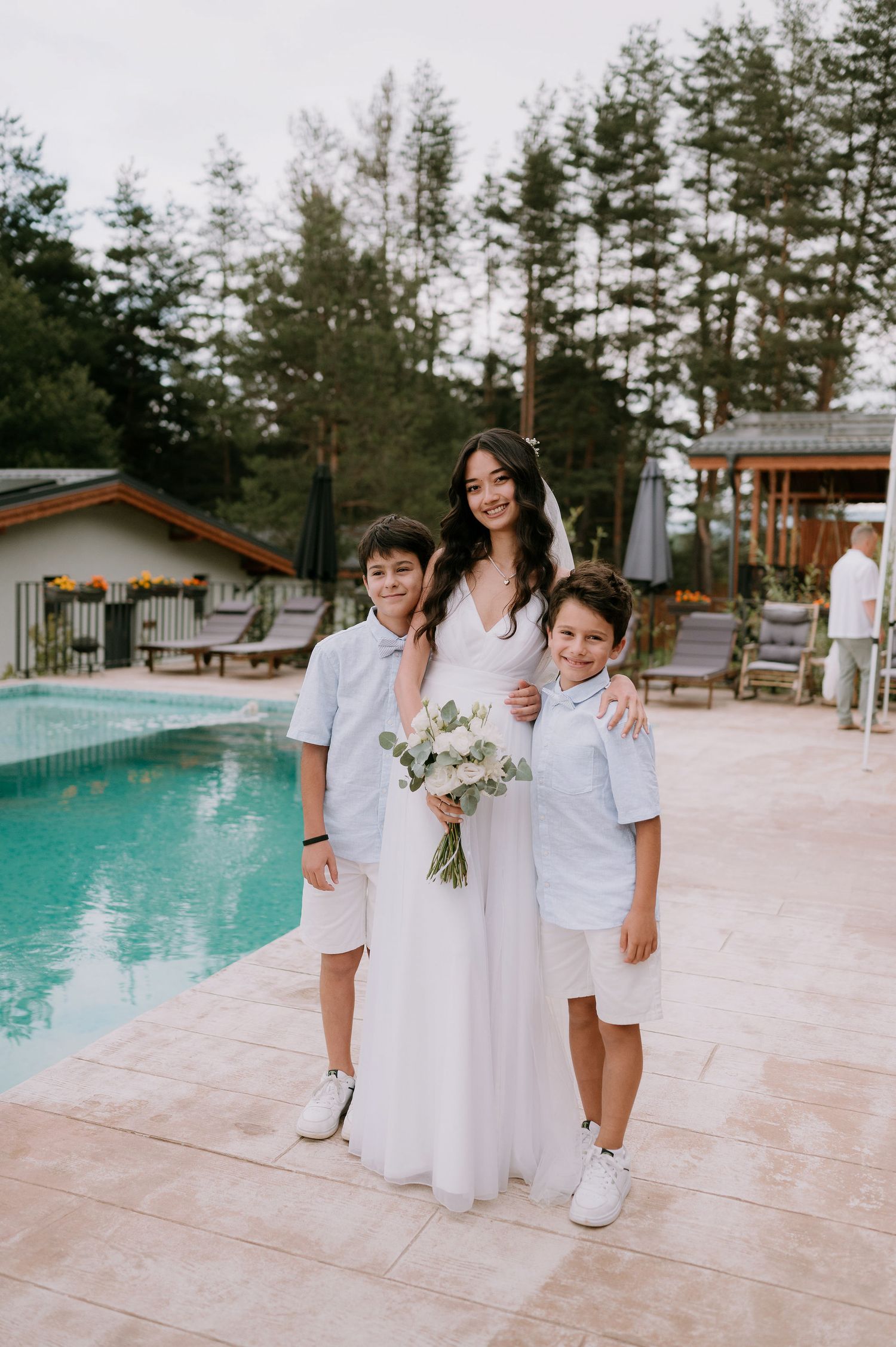 Wedding party in white attire posing by a pool with mountain views.