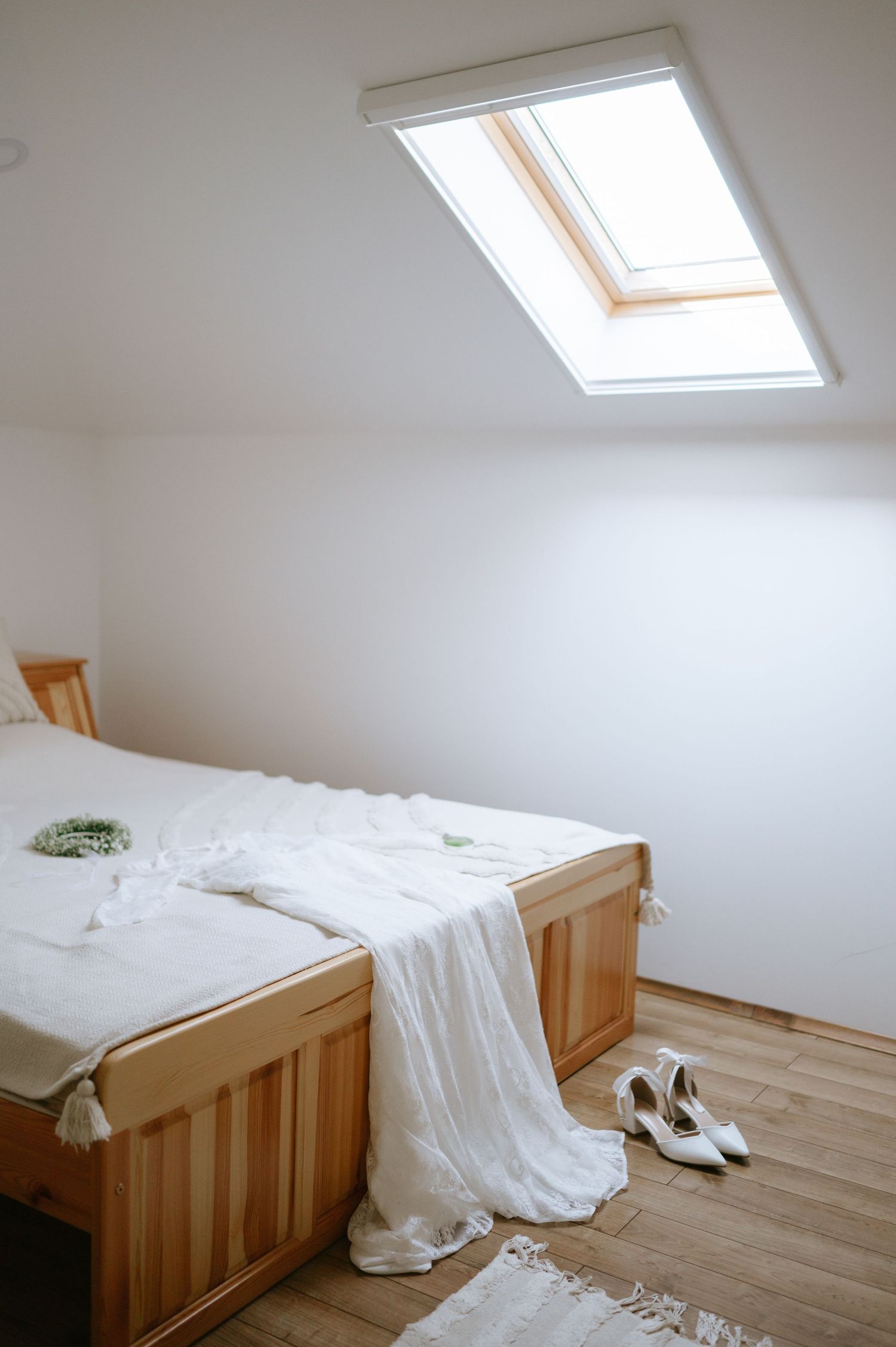 Minimalist attic bedroom with skylight window, wooden bed frame, and white bedding.
