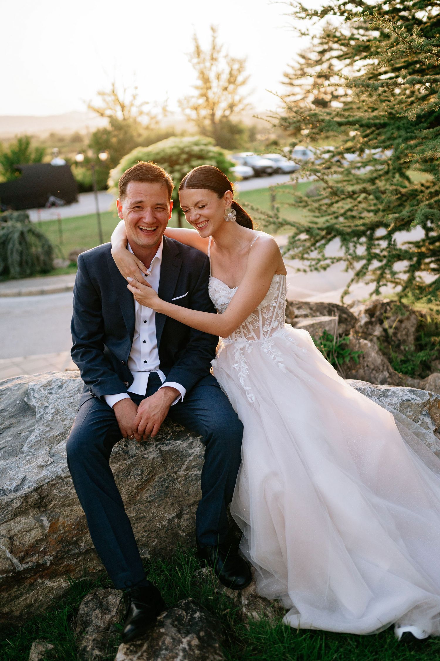 Candid wedding portrait captures natural laughter between couple on garden rocks.