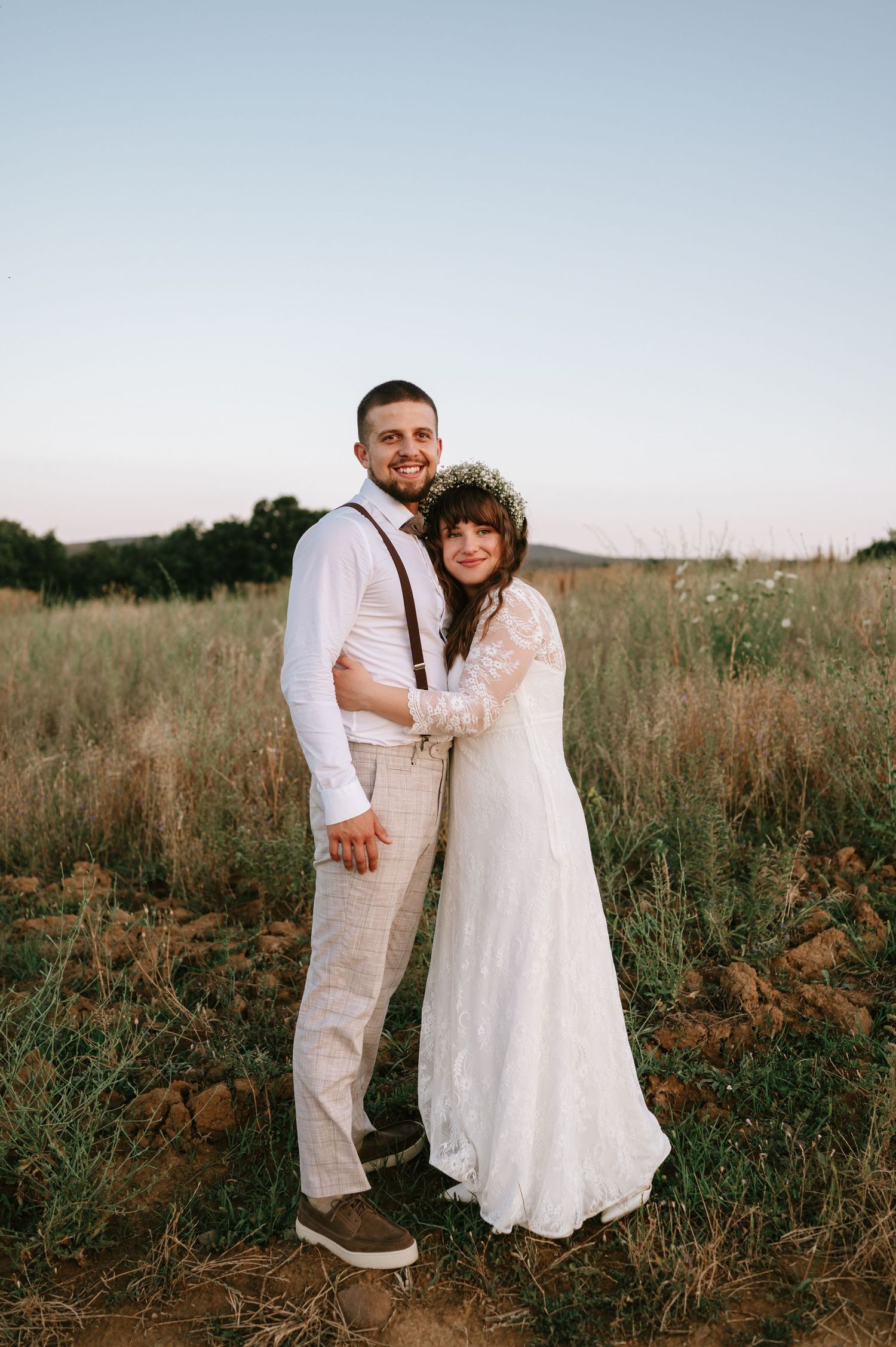 A couple poses together in a rustic field during sunset.