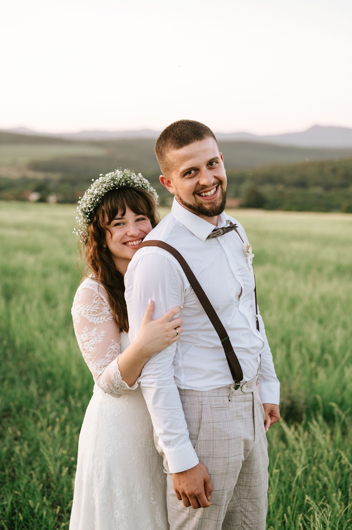 A joyful wedding couple poses together in a mountain meadow during golden hour.