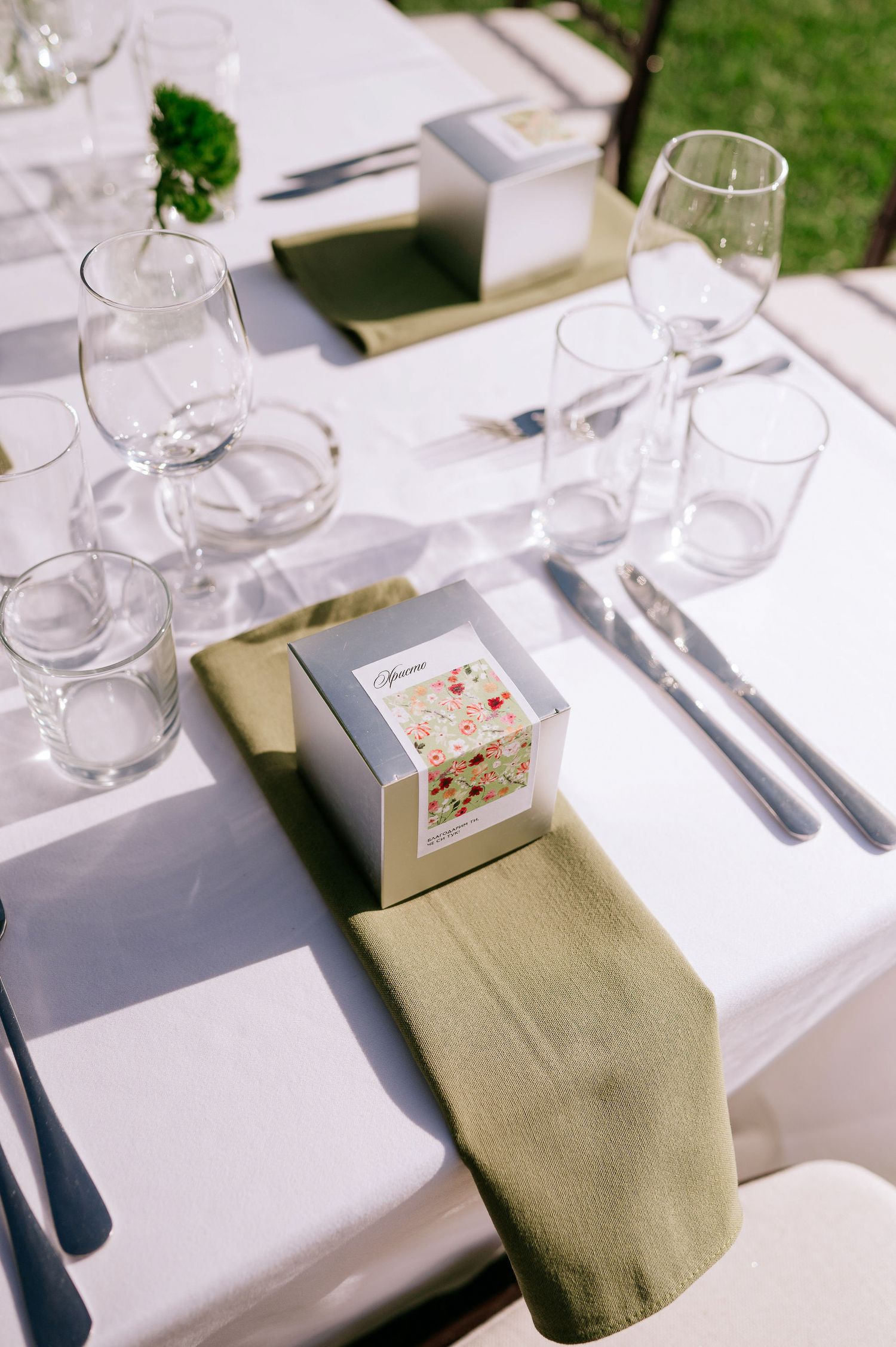 Elegant place settings with white linens, glassware, and sage green napkins for a formal event.