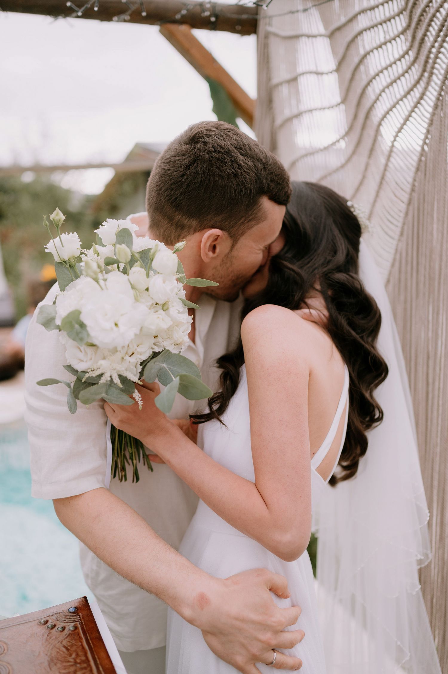 Romantic poolside wedding scene with white floral bouquet and macrame details.