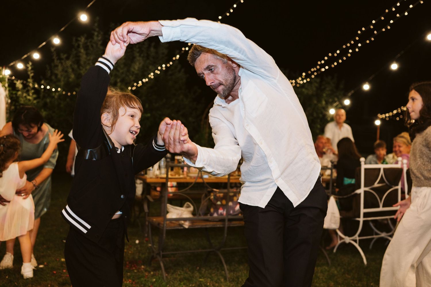 Two people dance energetically under string lights at an outdoor celebration.