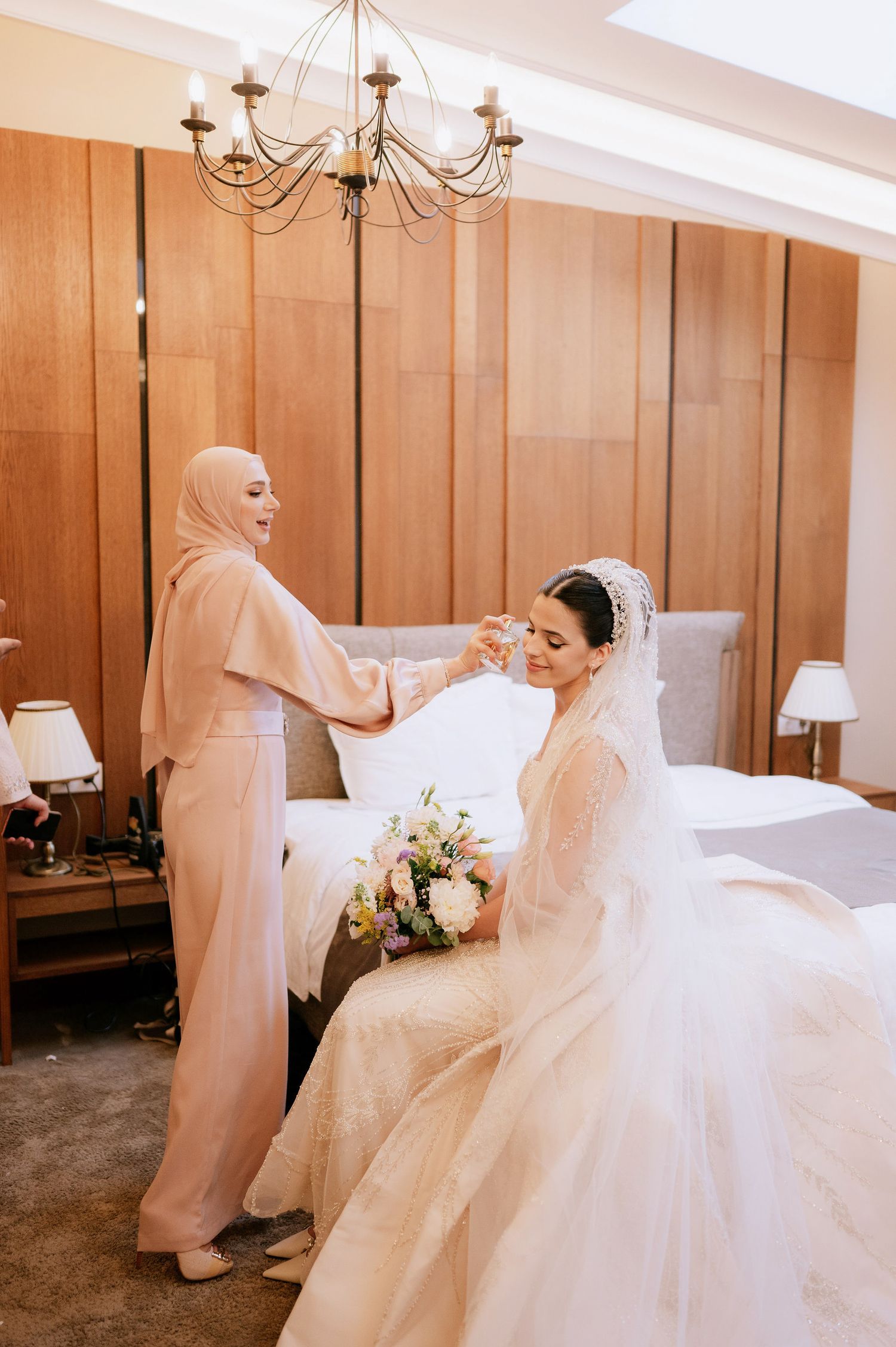 A bride in a voluminous white gown poses in a room with wood-paneled walls and chandelier lighting.