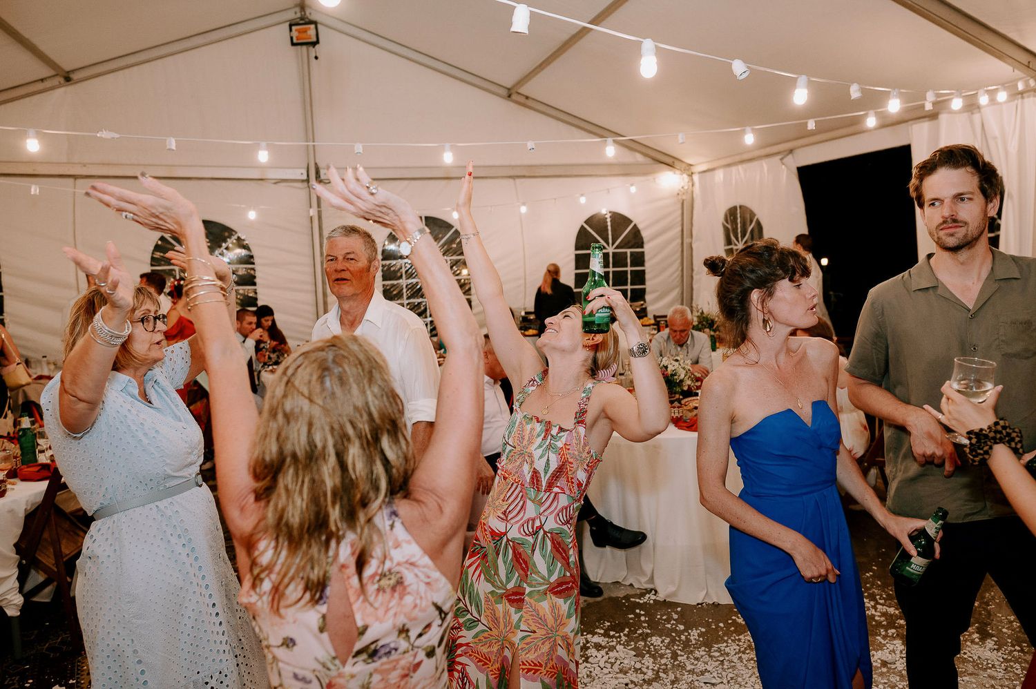 Wedding reception guests dancing and celebrating under string lights in a tent venue.