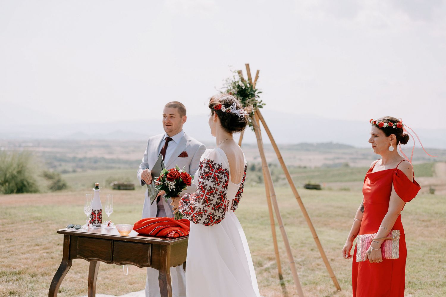 An outdoor wedding ceremony setup with wooden triangle arch and red accents against a scenic landscape.