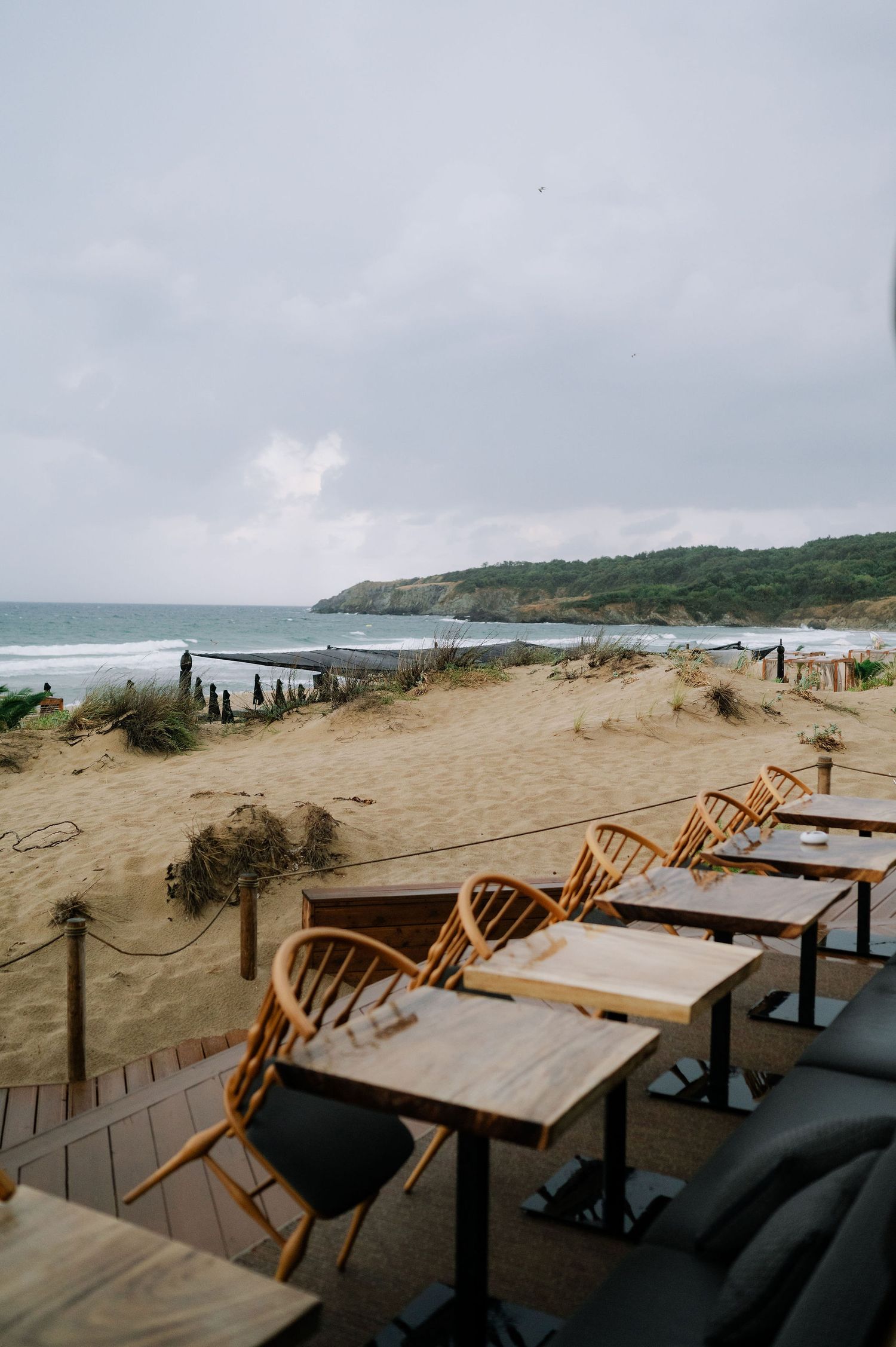 Empty oceanside restaurant tables and chairs overlooking a scenic beach and coastline.