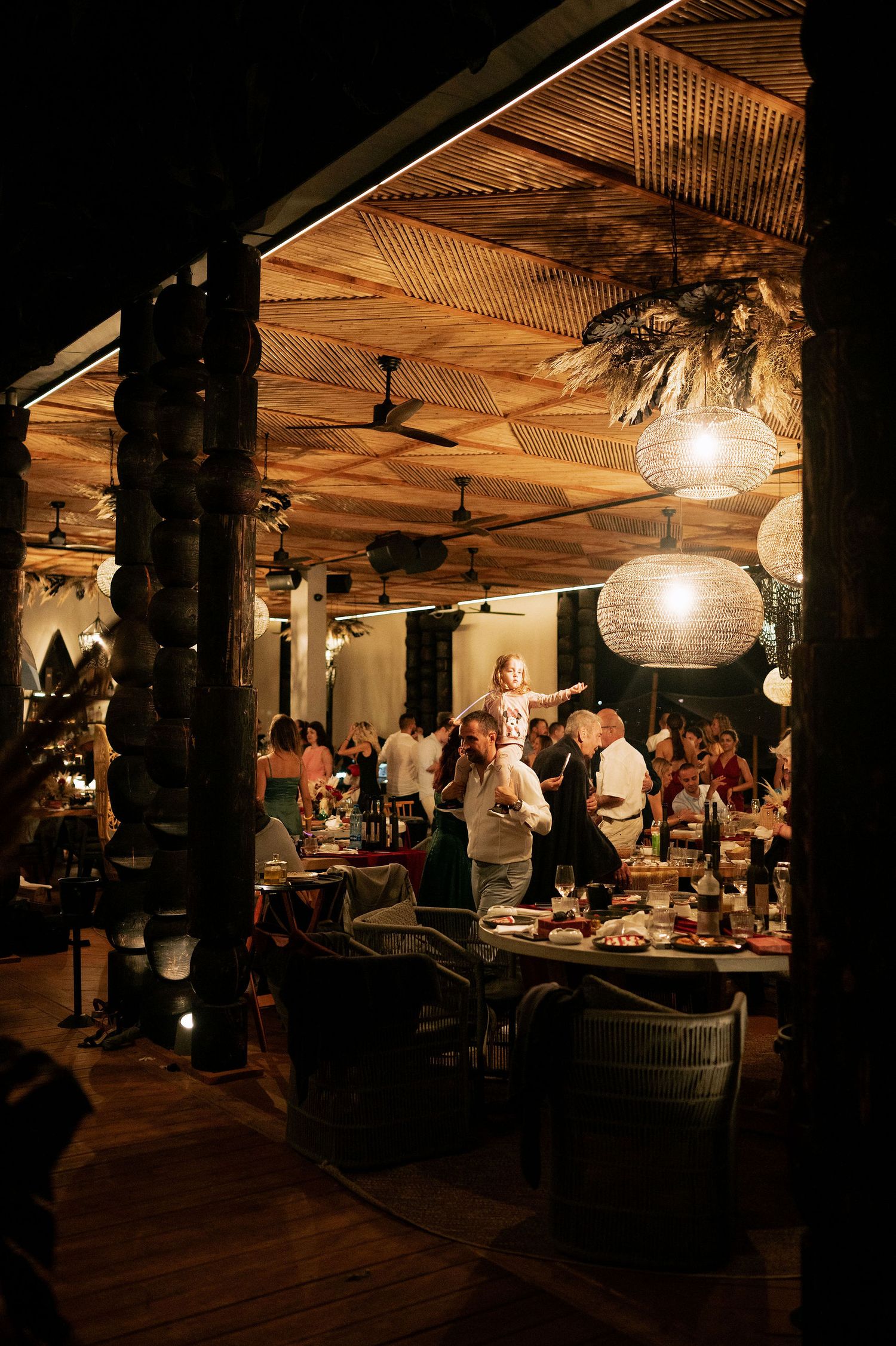 Rustic indoor venue with bamboo ceiling, pendant lights and guests dining at tables.