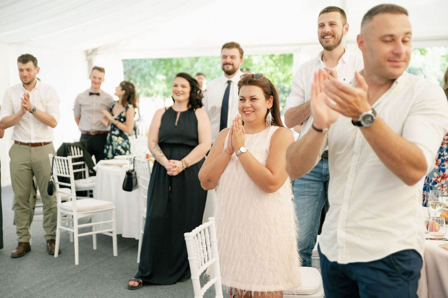 Wedding guests mingling and socializing in a white tent reception space.