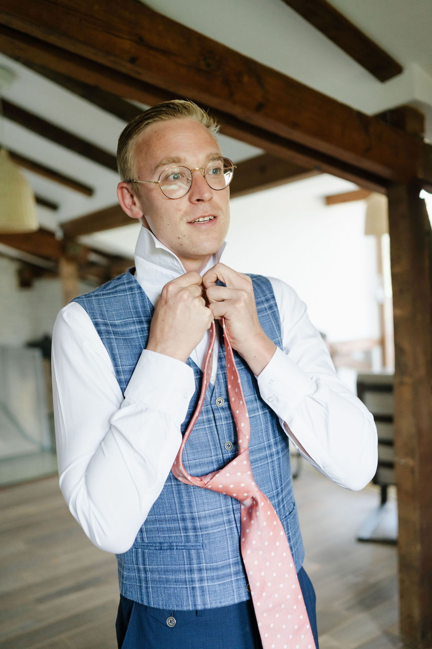 Person in formal attire adjusting their collar in a room with wooden beams.