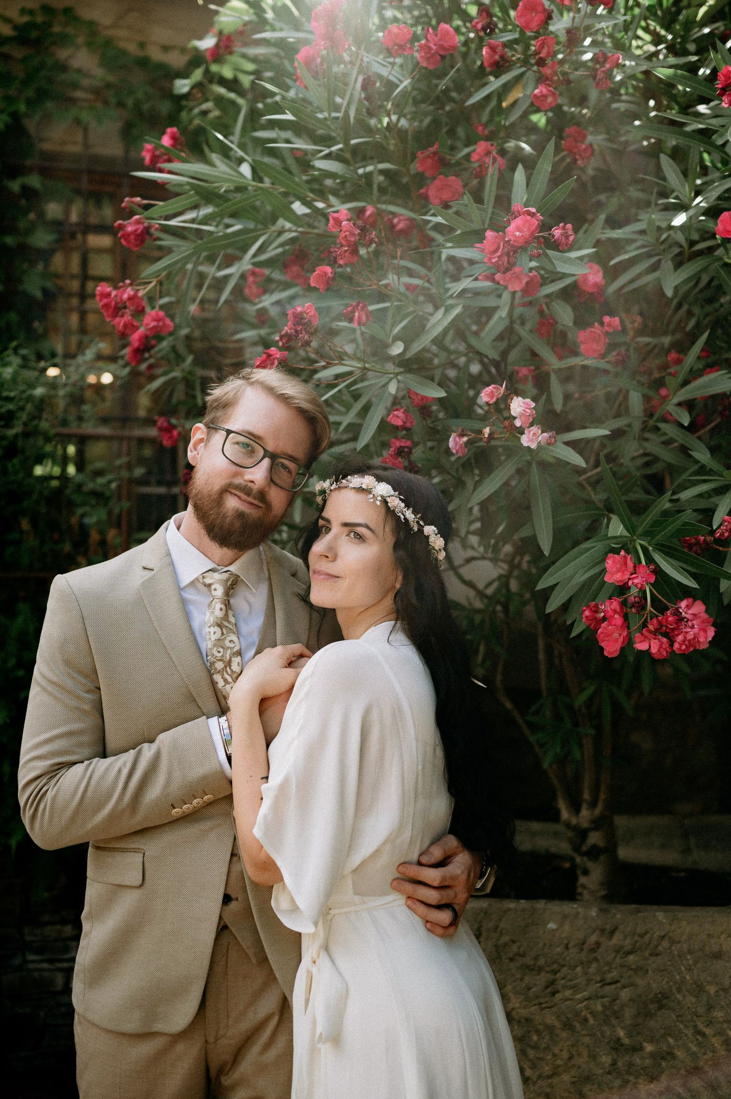 Playful wedding couple sharing a joyful moment among red flowering bushes.