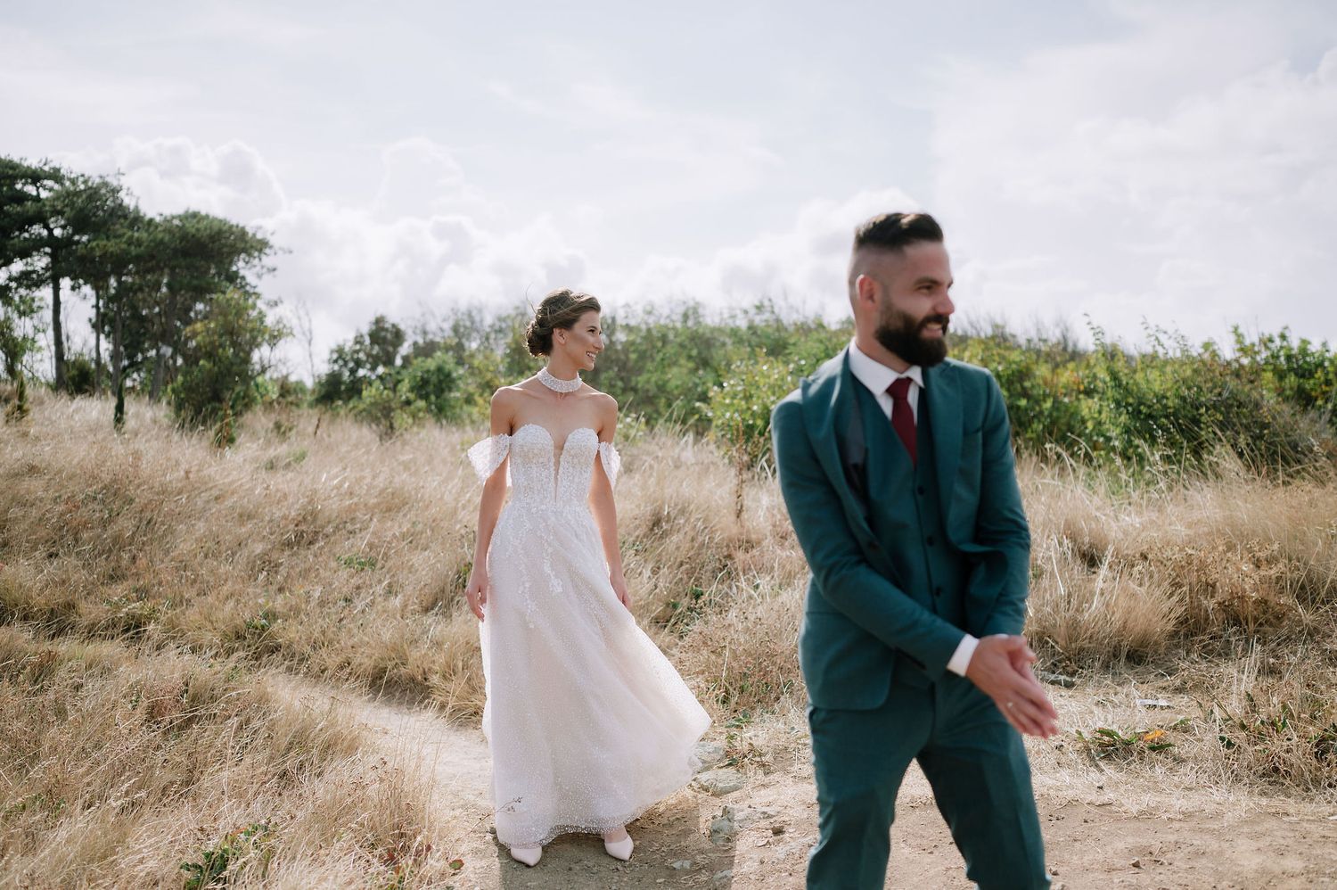 A couple in wedding attire walking along a scenic hilltop trail.