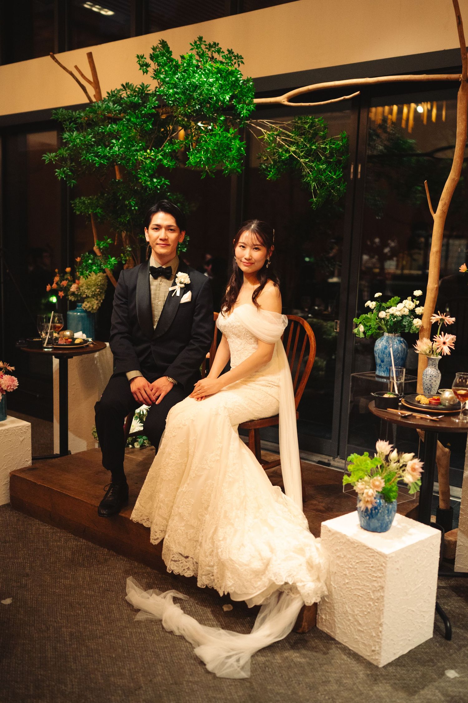 A wedding couple sits for portraits under an illuminated green tree display.