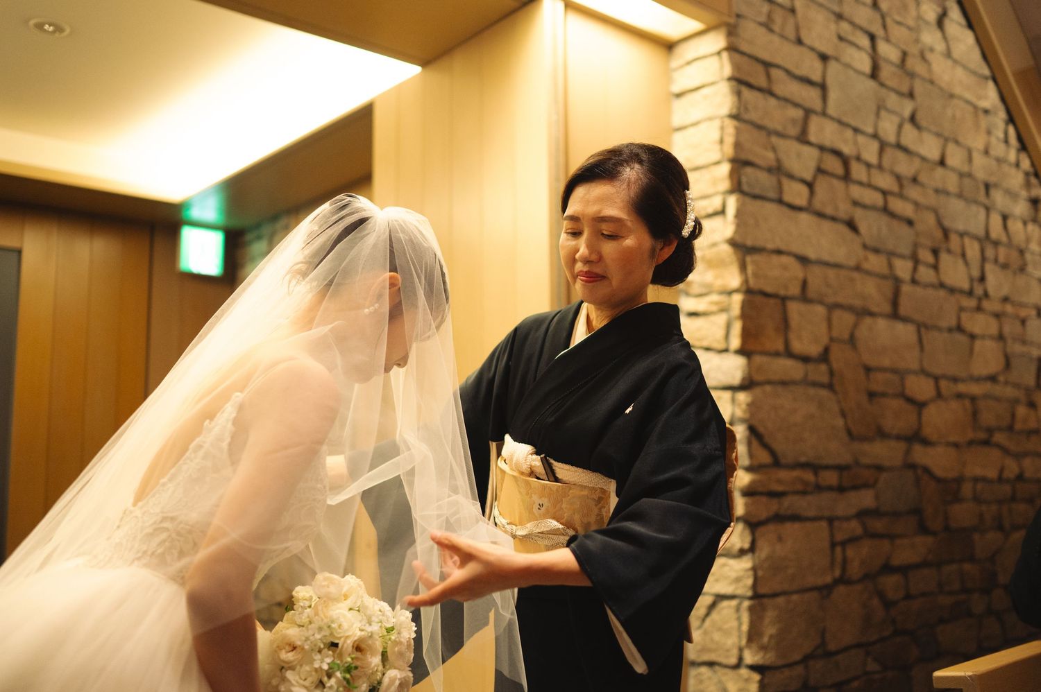 Wedding preparation moment as attendant adjusts bride's elaborate white veil and gown.