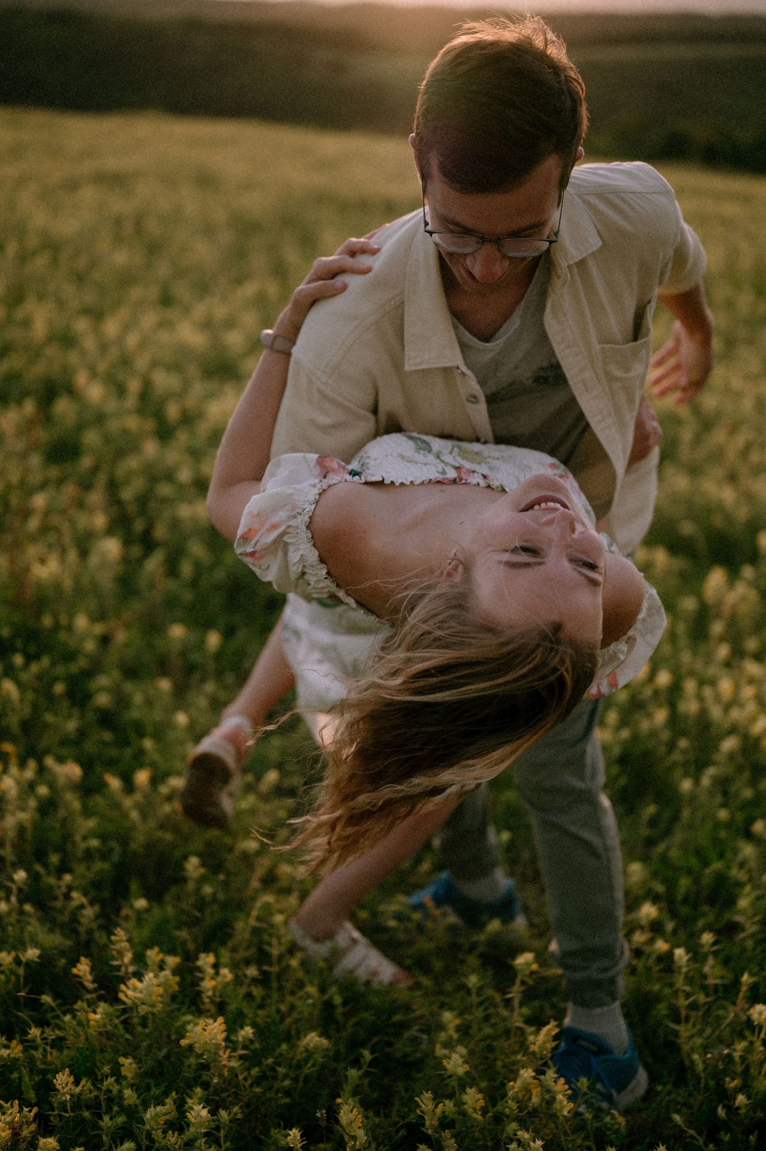 A romantic dip pose captured in a field of yellow flowers at dusk.