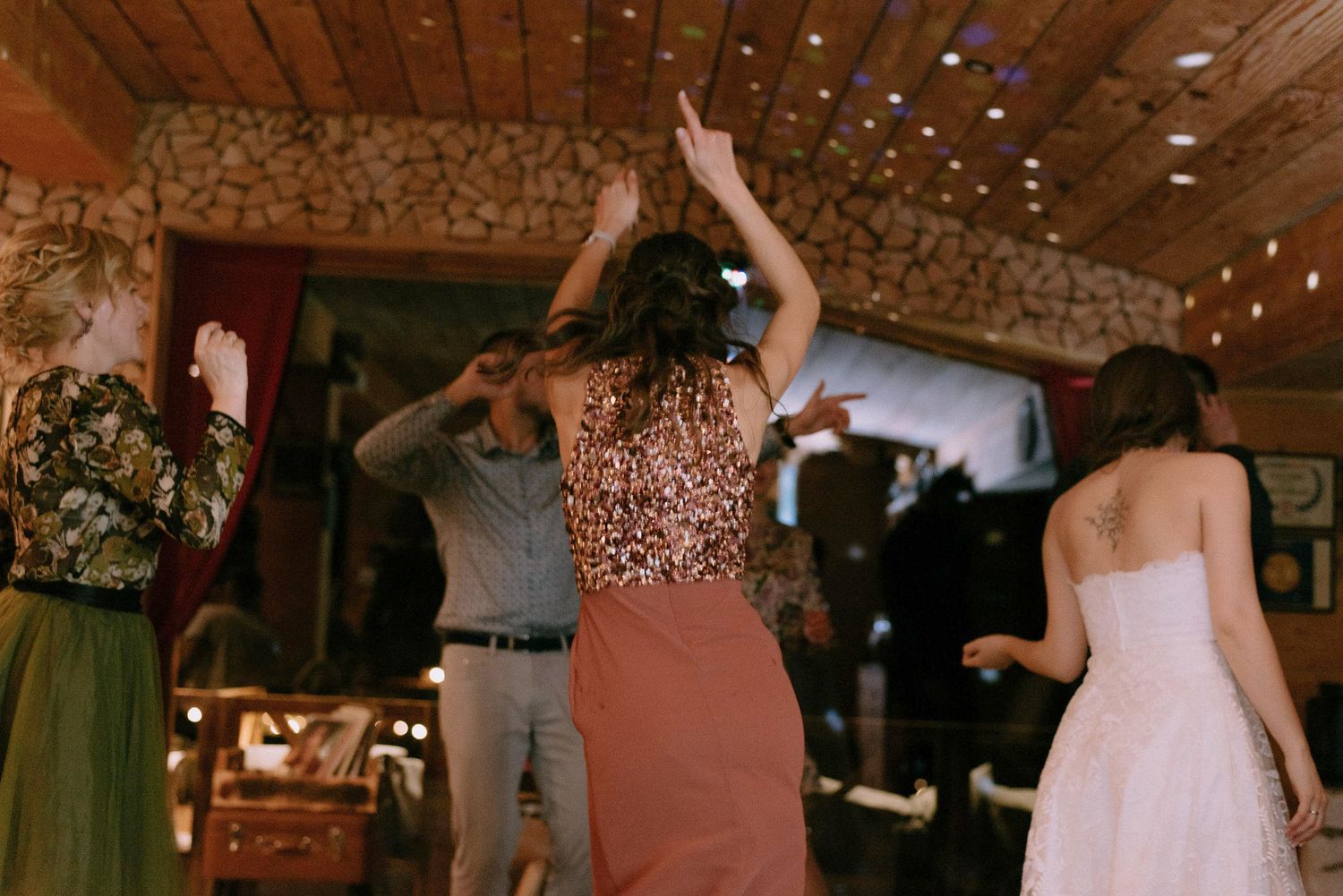 Wedding guests dancing and having fun on a wooden dance floor under string lights.