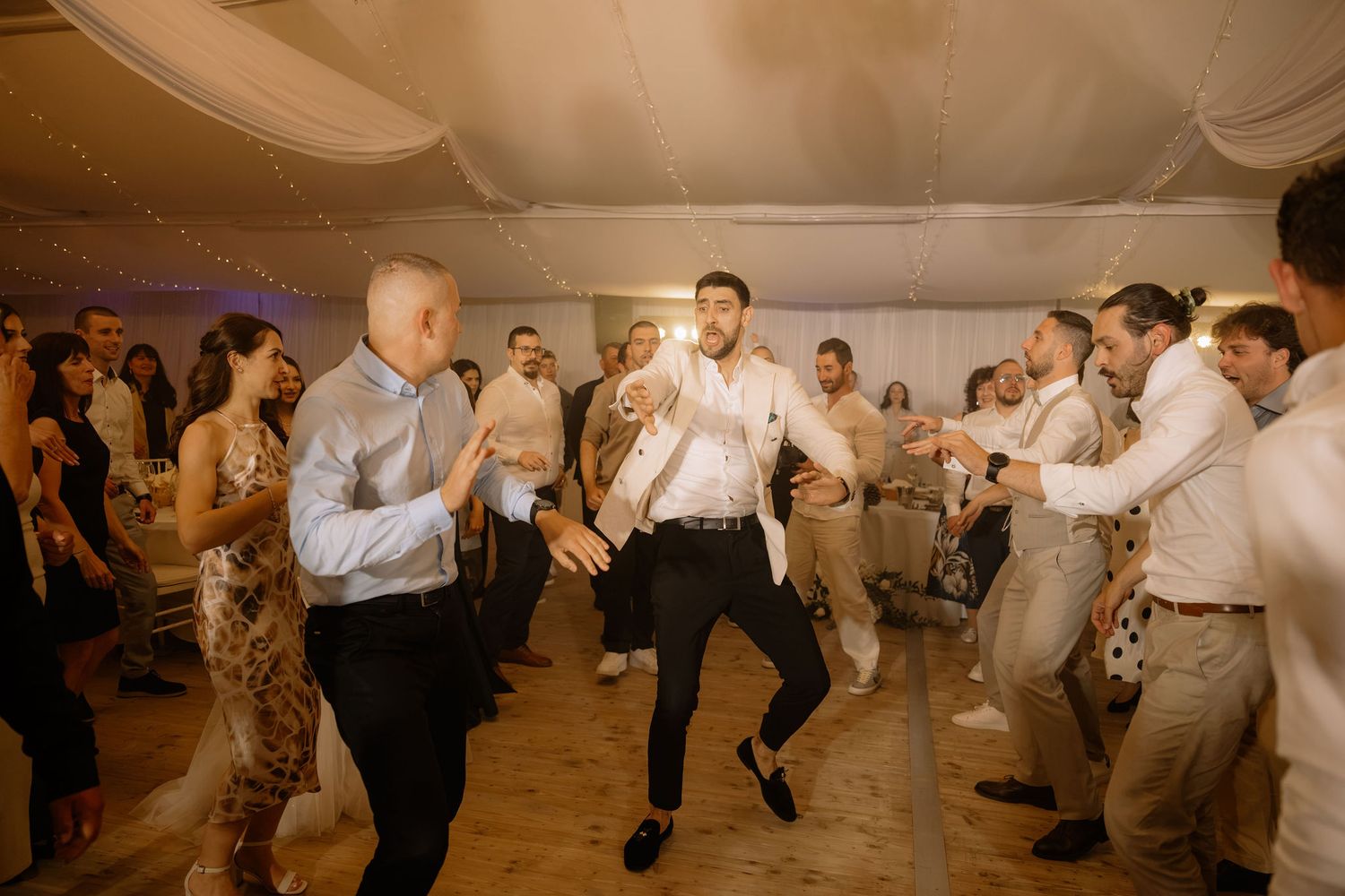 Guests dancing energetically at a wedding reception in a decorated tent venue.