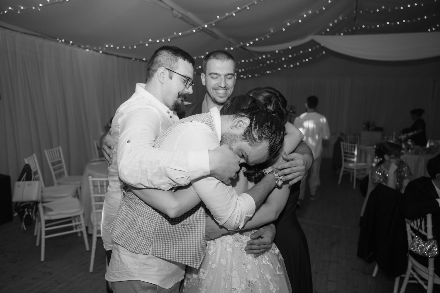 Black and white wedding reception photo of three people sharing a warm group hug on the dance floor.