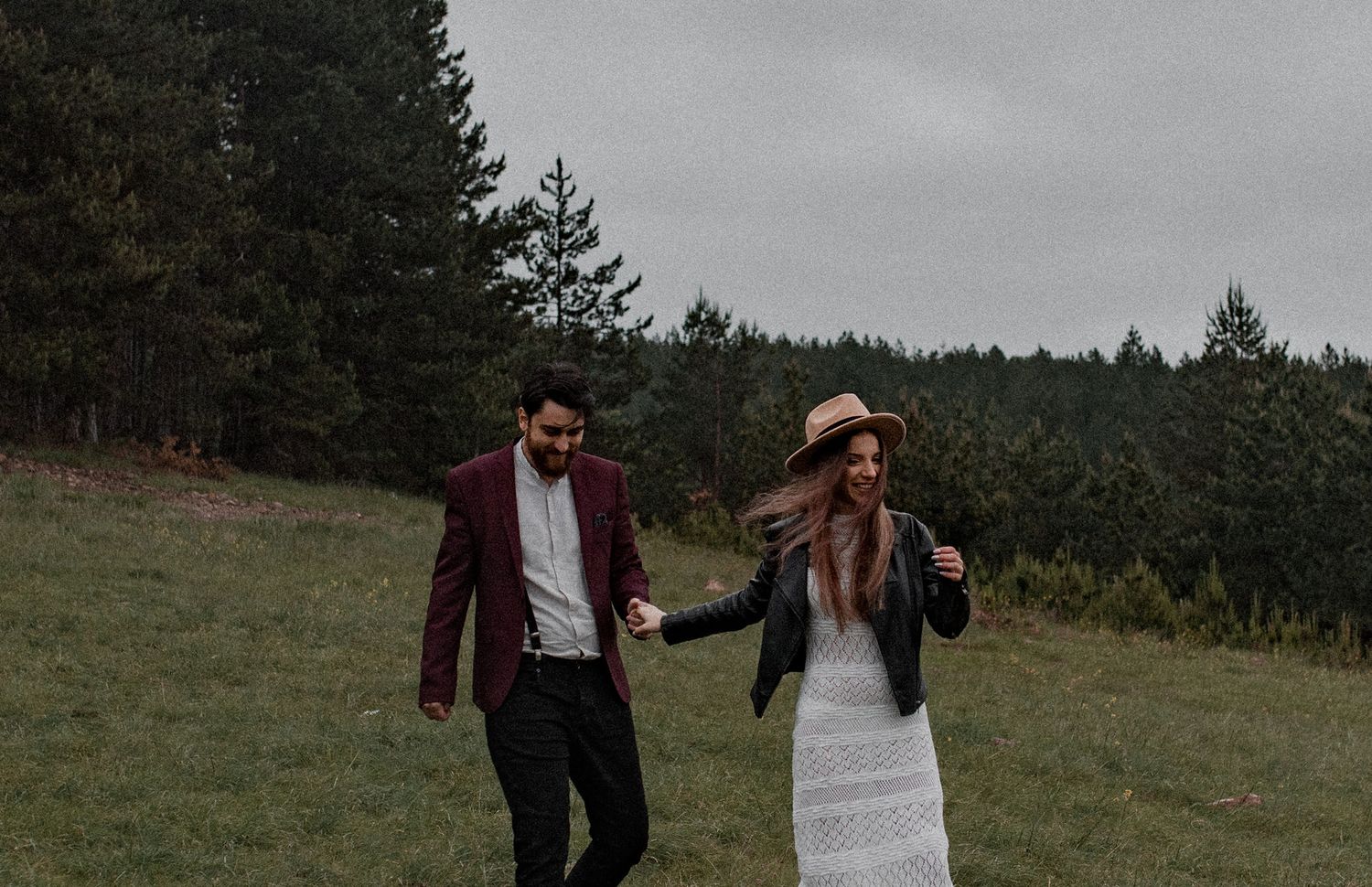 Couple walking together through evergreen forest on a misty mountain trail during a cloudy day.