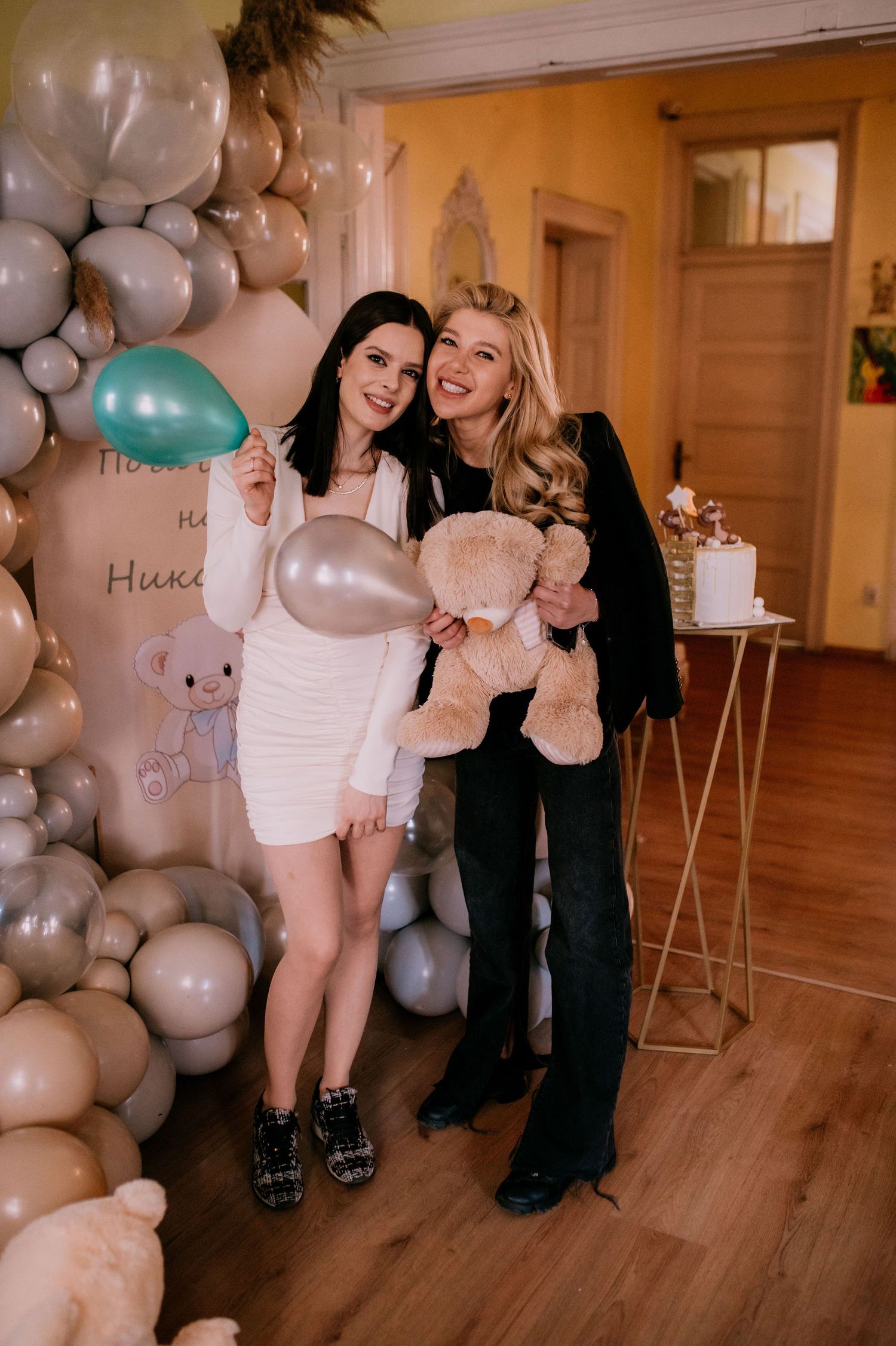 A celebratory event space decorated with elegant white and silver balloon arrangements on hardwood floors.