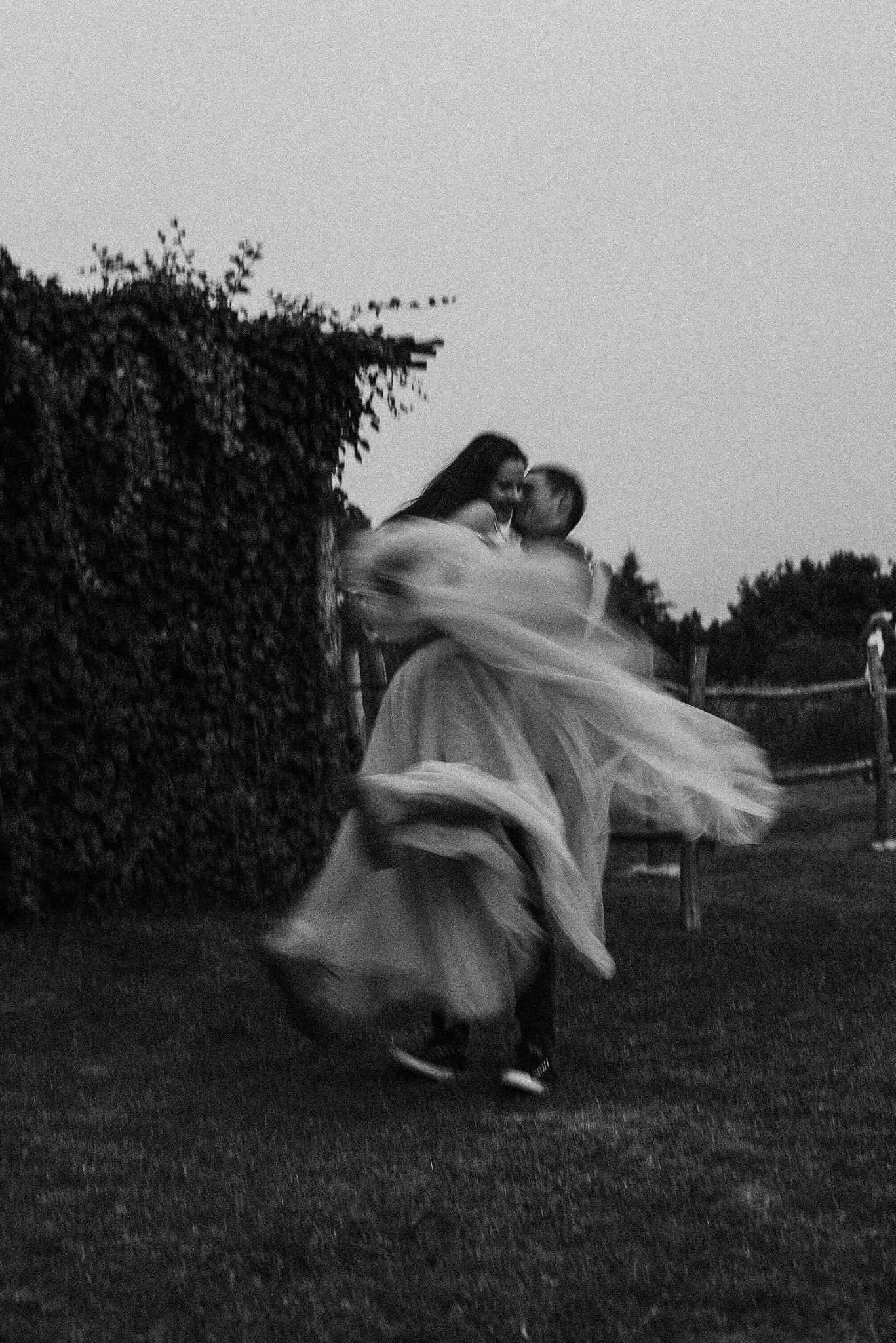 A sequence of black and white photos showing a figure in flowing fabric performing a twirling motion on grass.