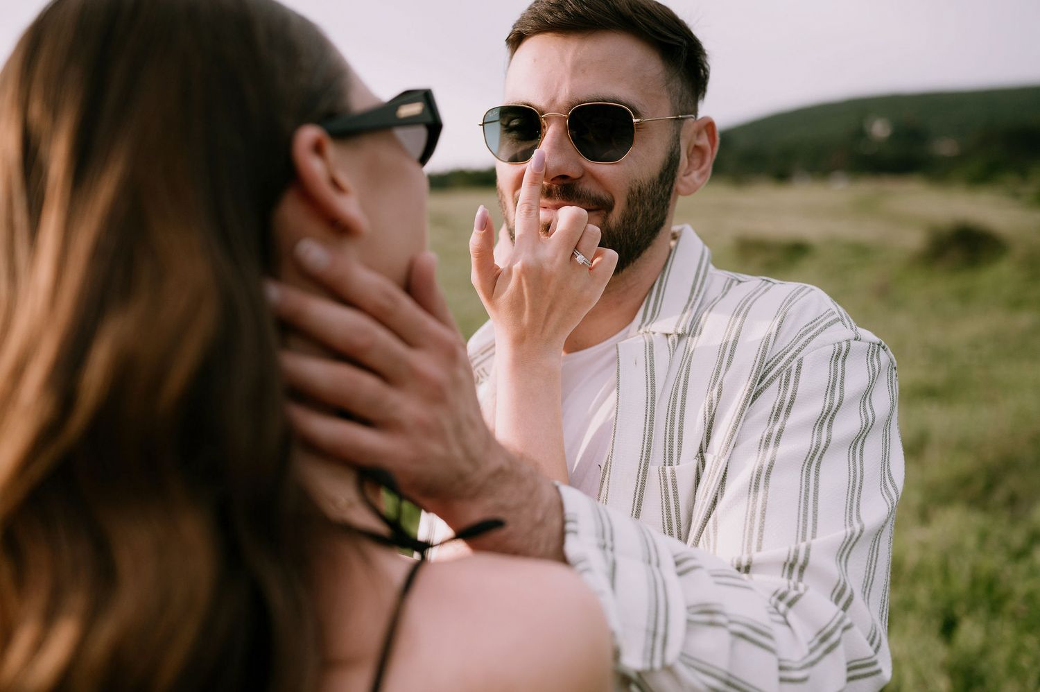 A couple in casual attire shares intimate moments in a sunny outdoor field setting.