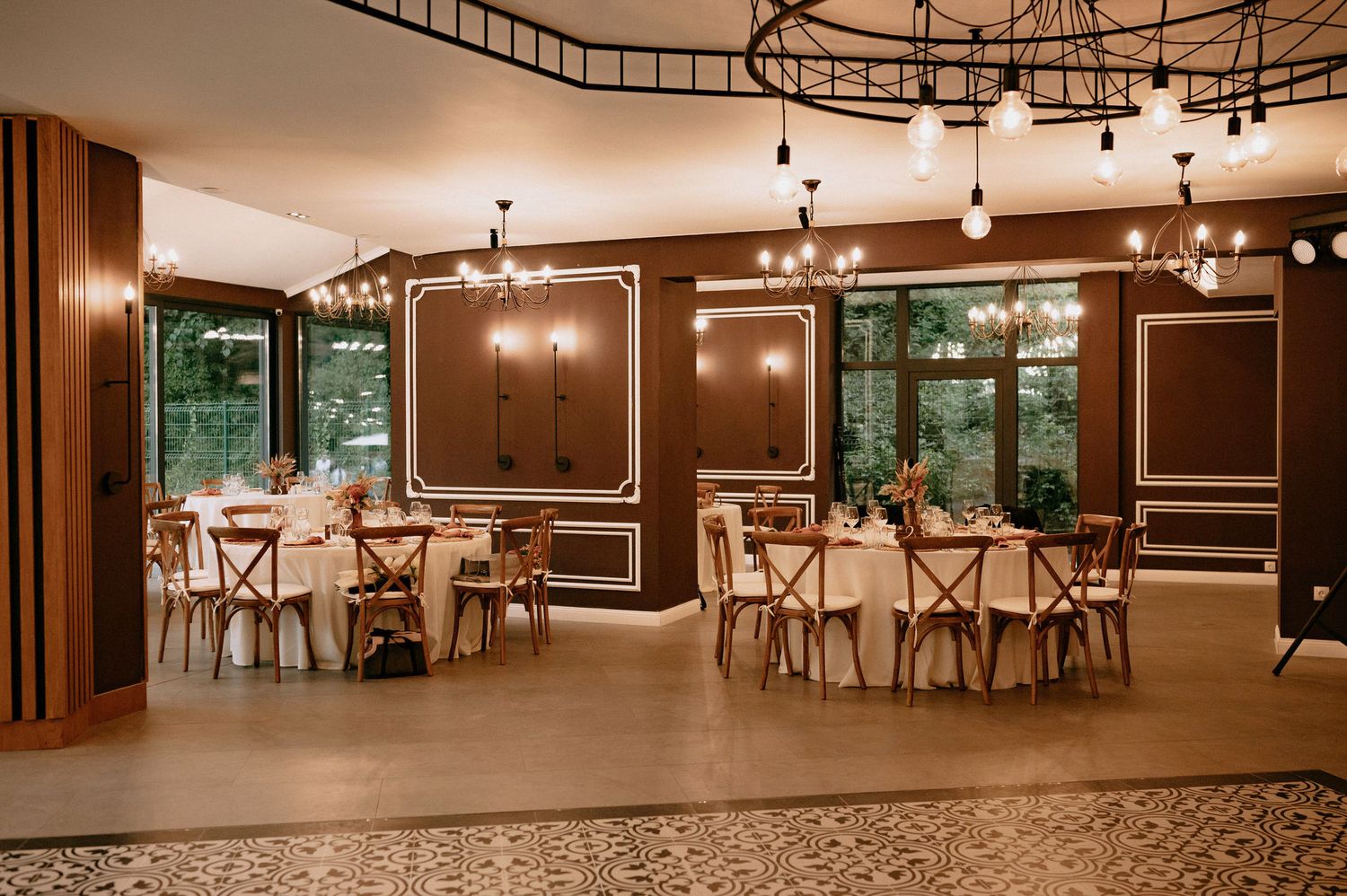 A panoramic view of an empty event space with rustic decor, wooden chairs, and warm lighting throughout.