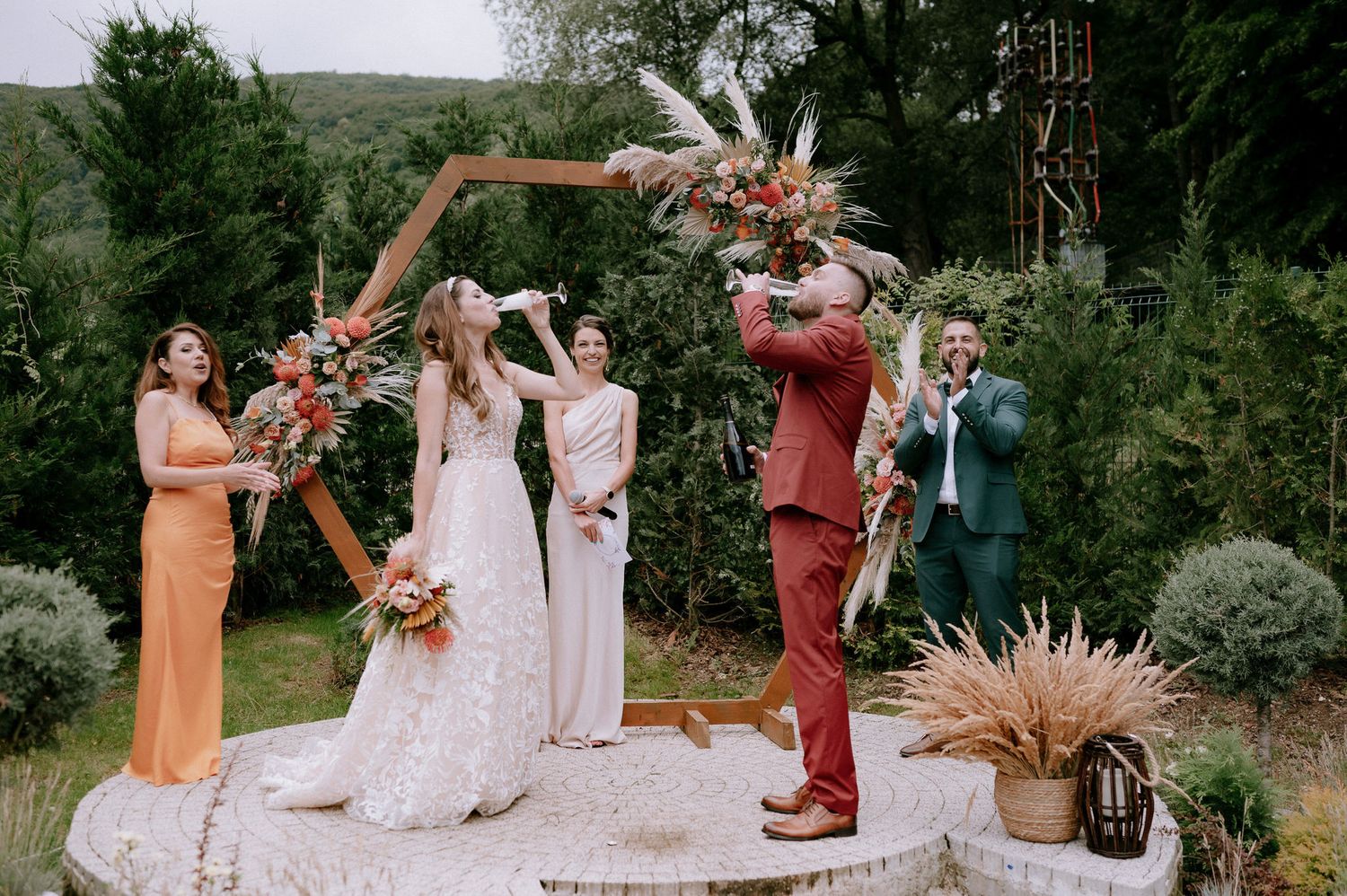 Wedding party celebrates with champagne spraying in an outdoor garden setting with lush greenery.