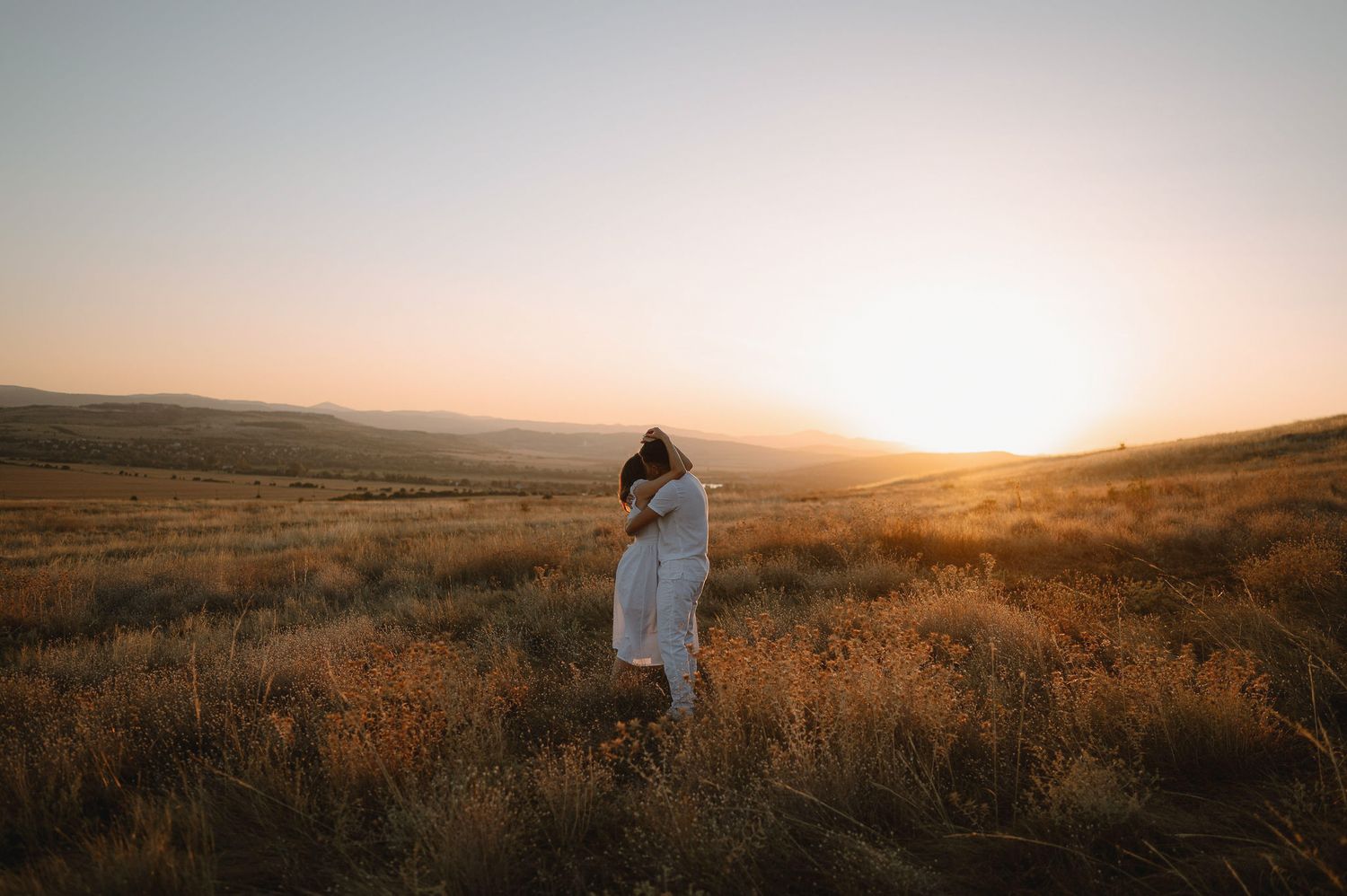 Silhouetted figures stand together in vast prairie field during golden hour sunset.