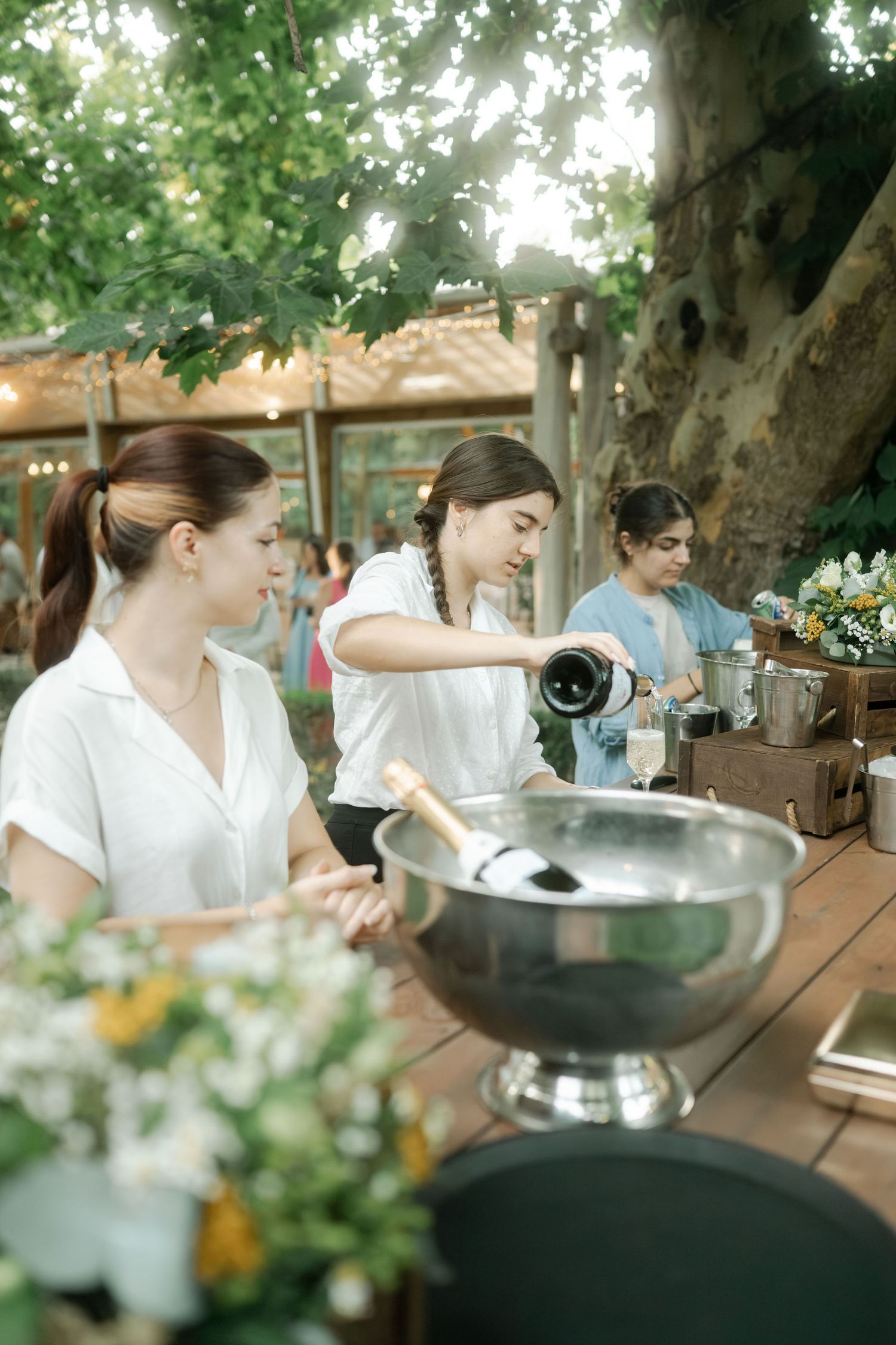 People gather around a fondue pot at an outdoor restaurant table on a sunny day.