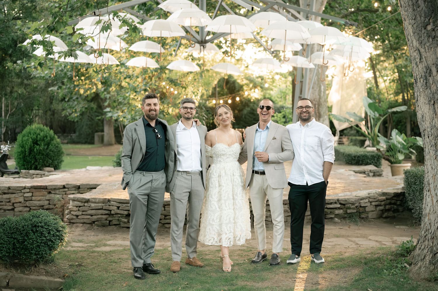 Wedding party walking in a line through a garden setting at sunset with trees and greenery in the background.
