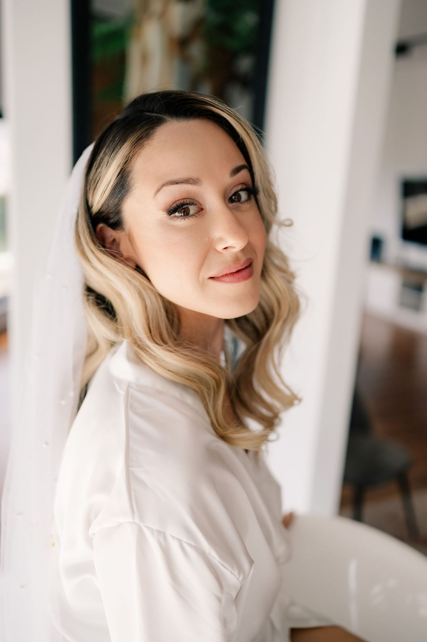 Woman in white sweater posing against bright interior background in soft natural lighting.