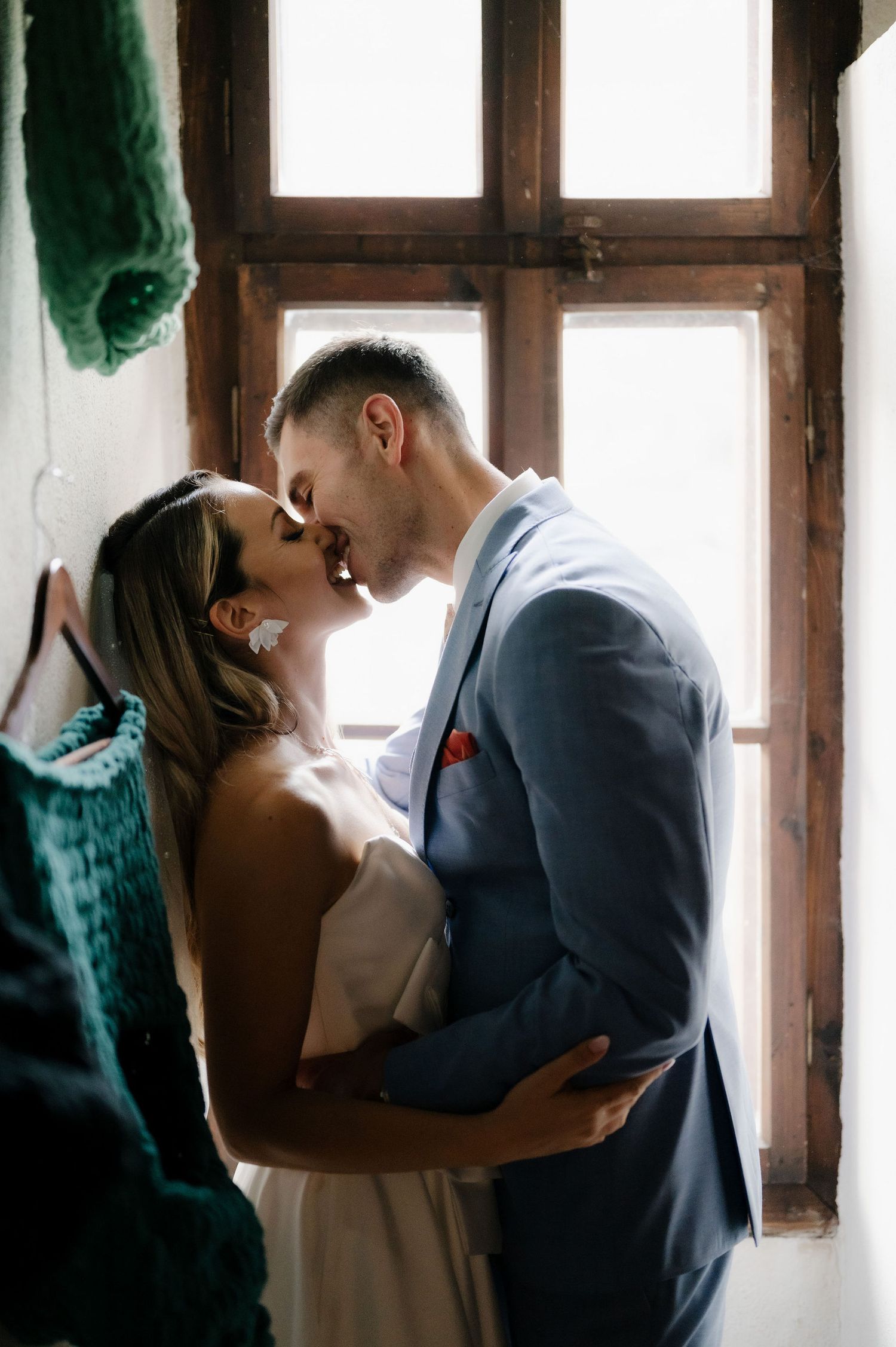 A romantic couple shares an intimate moment near a window in soft natural lighting.