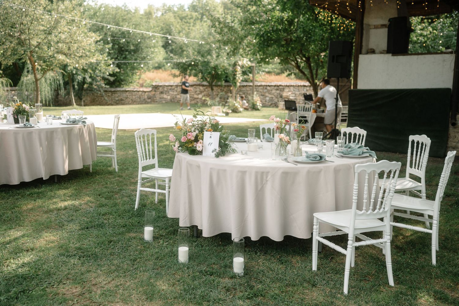 Elegant outdoor wedding reception setup with white chairs and tables arranged on a grassy lawn in natural lighting.