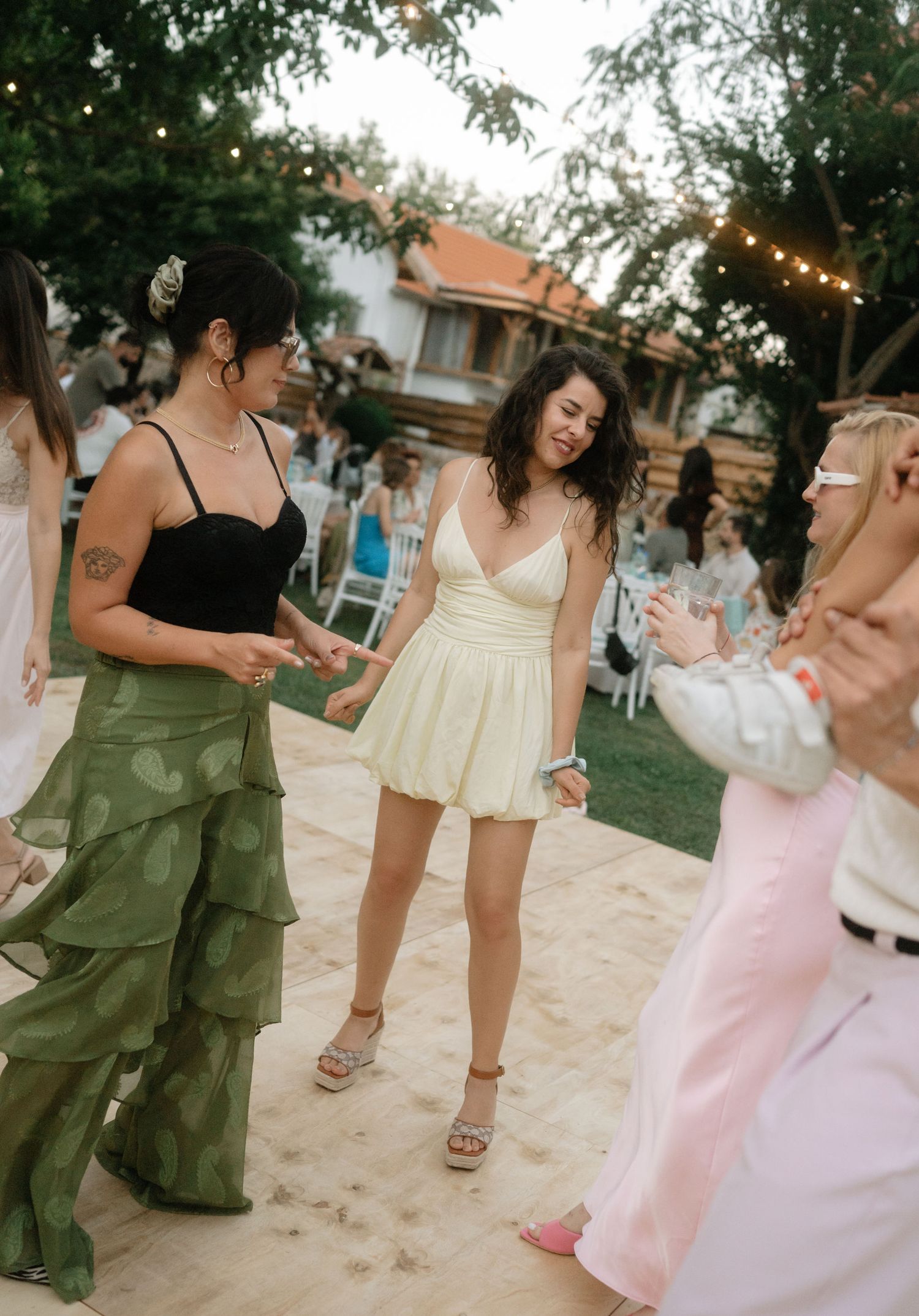 People dancing together at an outdoor summer party wearing flowy dresses in pastel and olive green colors.