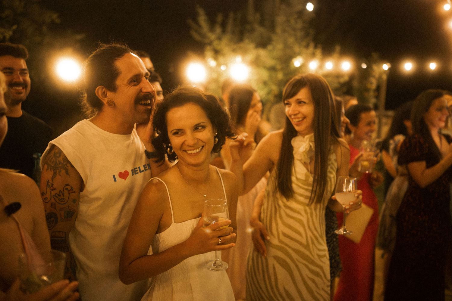 People enjoying drinks and conversation at a dimly lit evening party with warm ambient lighting.