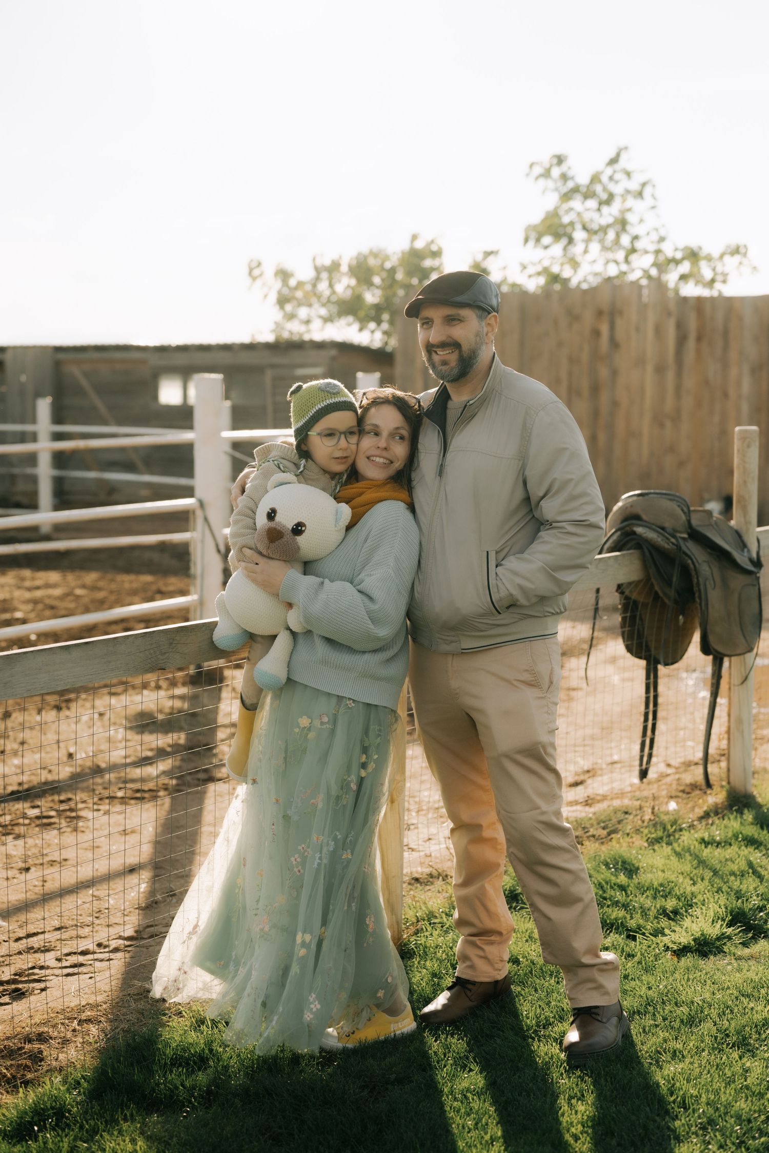 A couple poses together in a romantic outdoor setting with sunlight filtering through a rustic wooden fence.