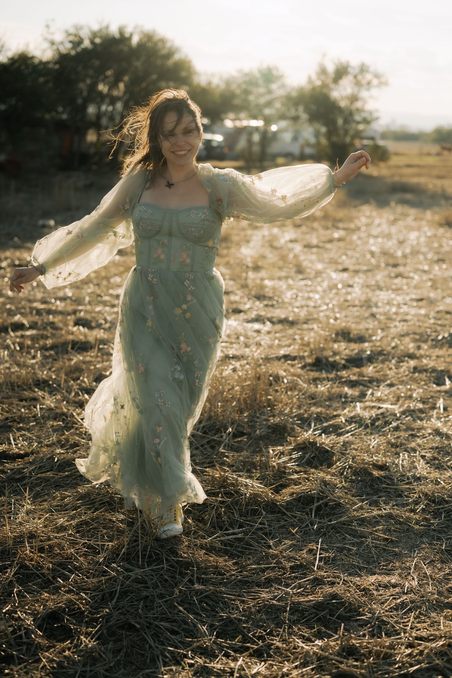 A person in a flowing light blue dress twirls joyfully in a sunlit field during golden hour.