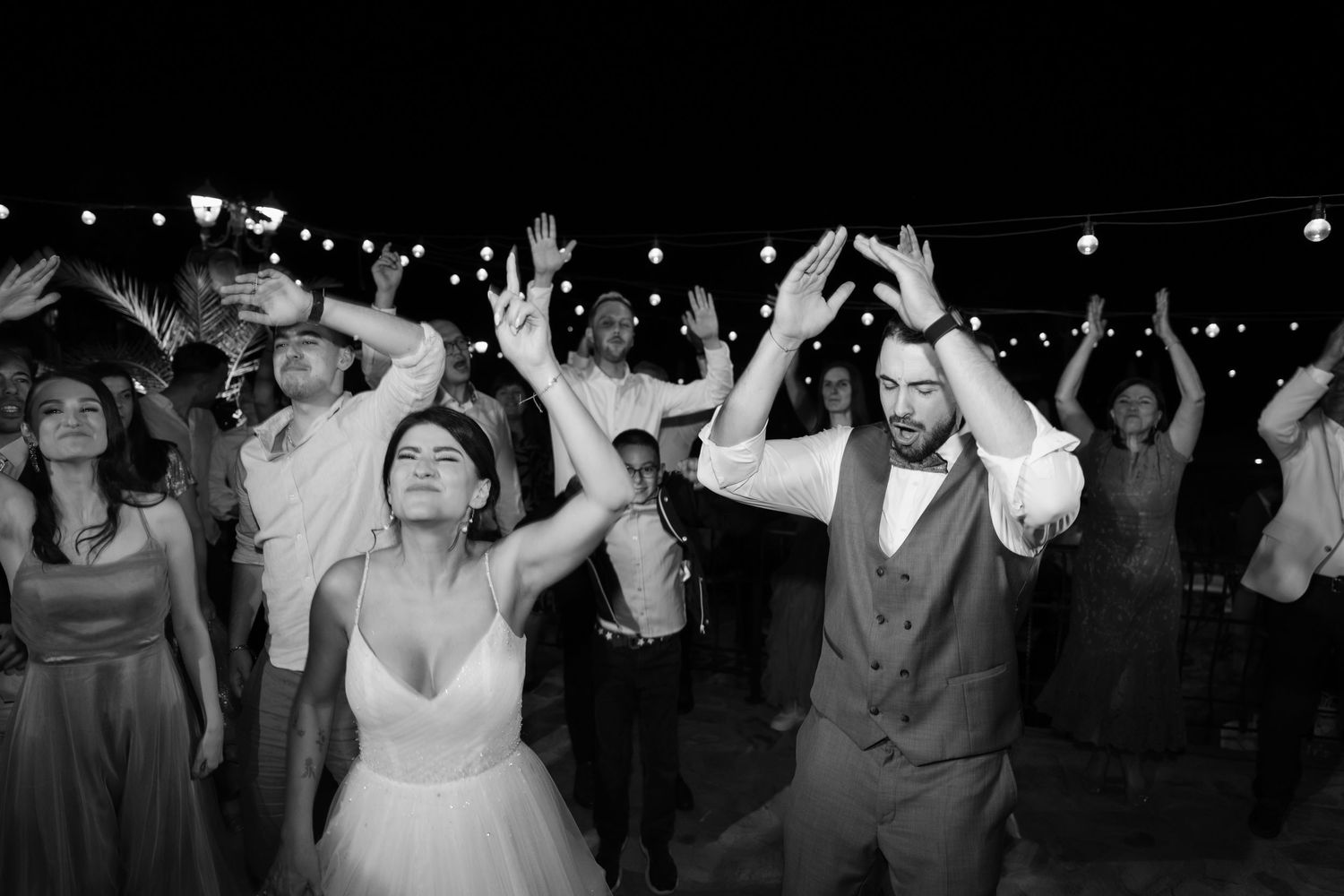 Wedding guests dance together on a dark dance floor during an energetic reception celebration.