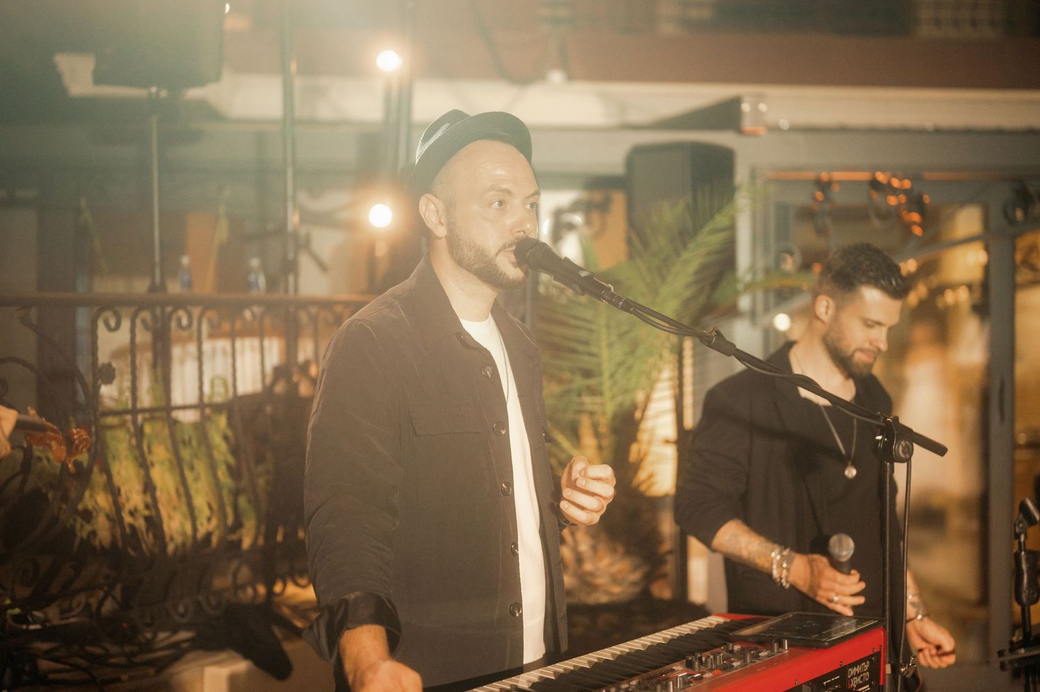 Musicians perform on stage with keyboards and electronic equipment in a dimly lit venue with ambient lighting.
