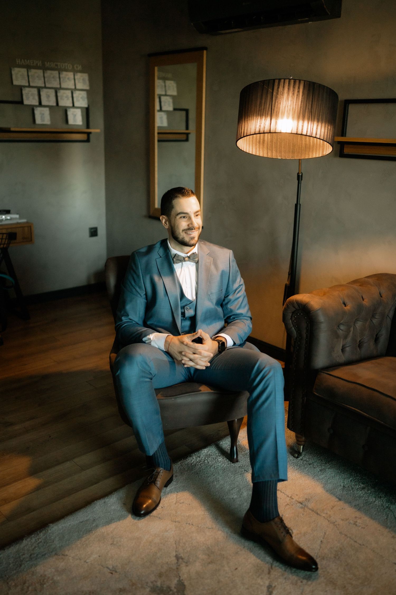 A person in a blue suit sits on the floor in a dimly lit room with hardwood floors and modern decor.