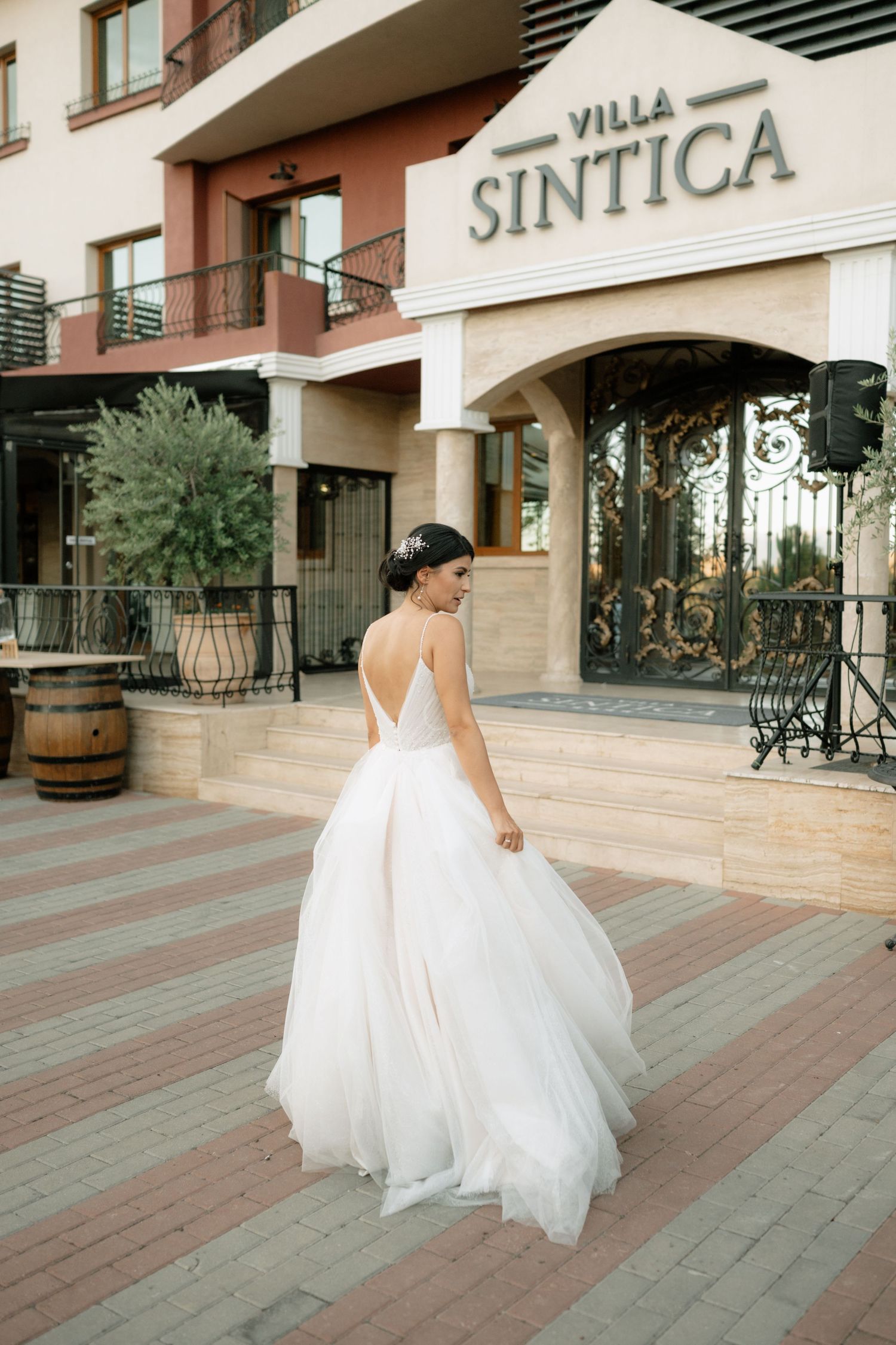 A bride in a flowing white wedding gown twirls on a paved terrace outside Villa Sintica.