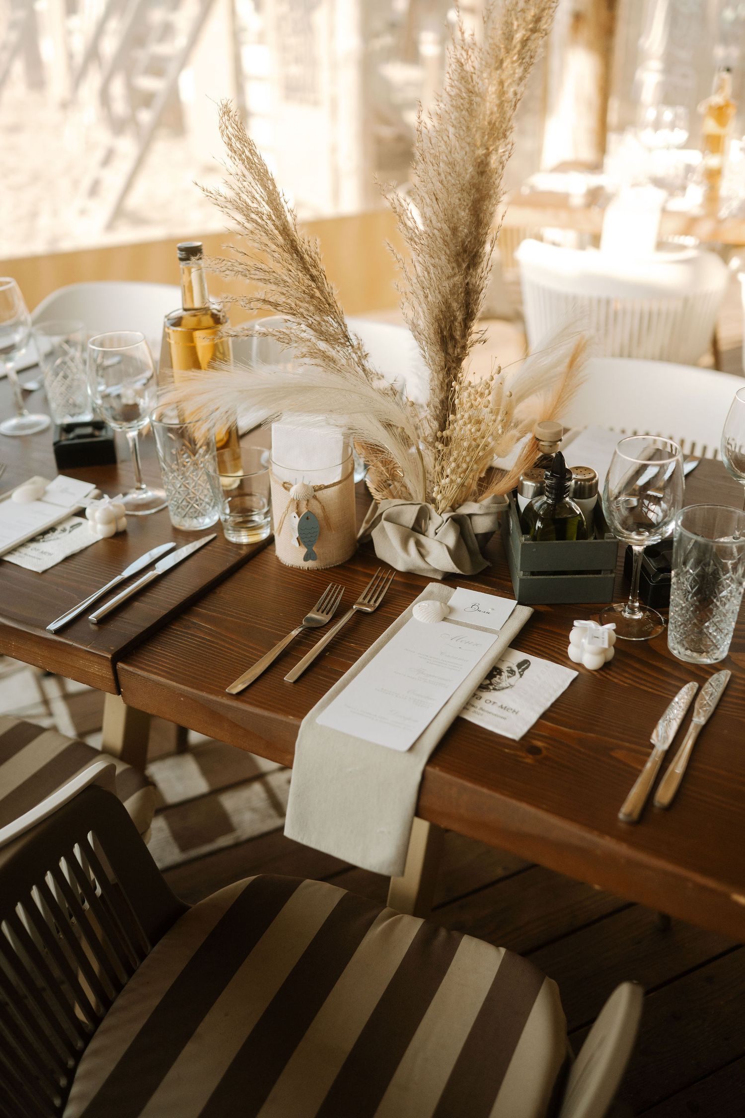 Elegant table setting with pampas grass centerpiece, wooden table, and place settings in warm lighting.